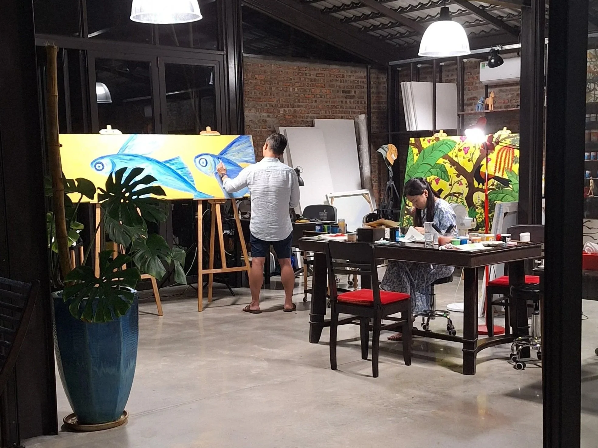 Two guests painting large colorful canvases at easels in The Interlude's open-air studio in the evening