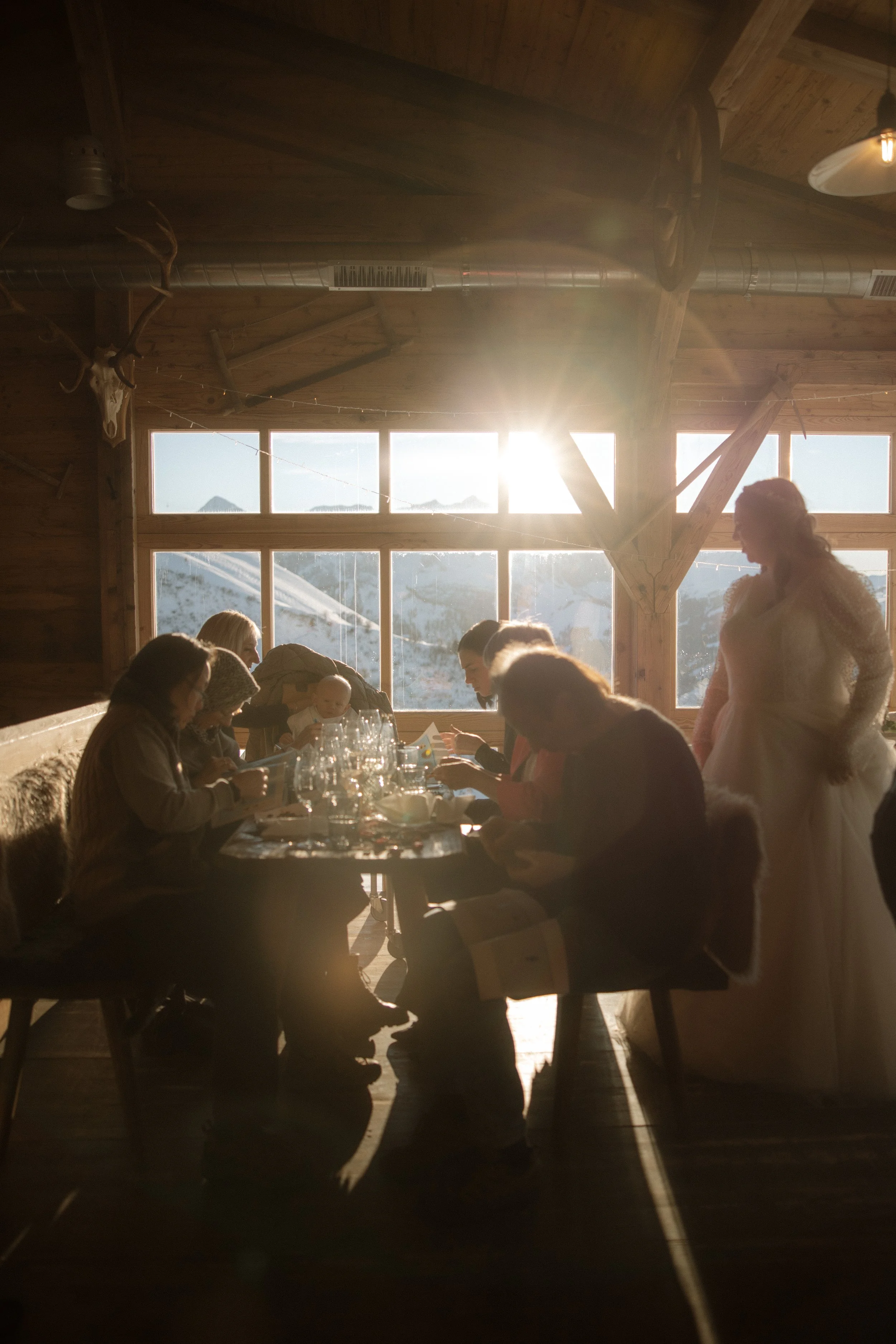 Menschen, die an einem Tisch in einer rustikalen Holzhütte sitzen, während die Sonne draußen bei Sonnenuntergang scheint.
