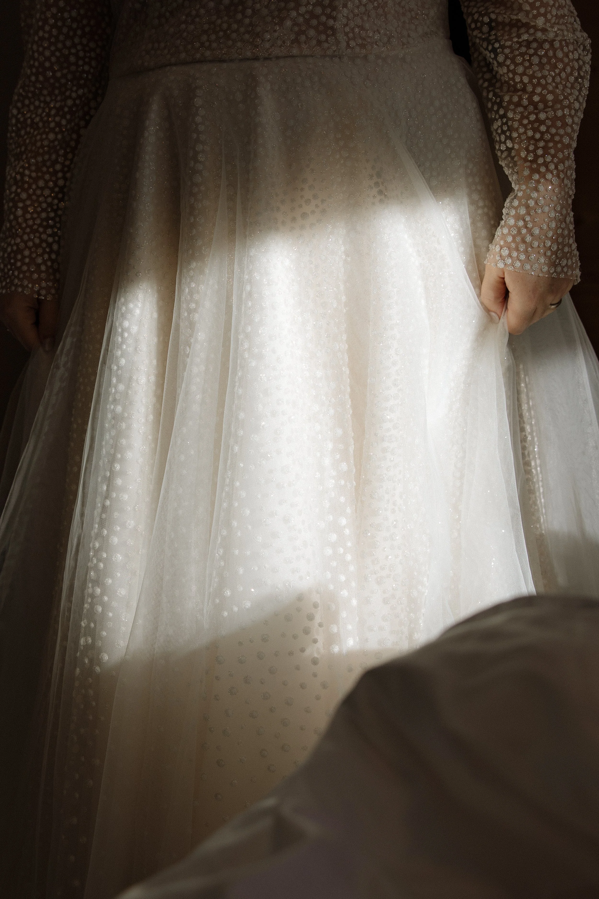 Nahaufnahme eines Brautkleides mit Perlenstickerei, gehalten von einer Person, die an der Seite steht.