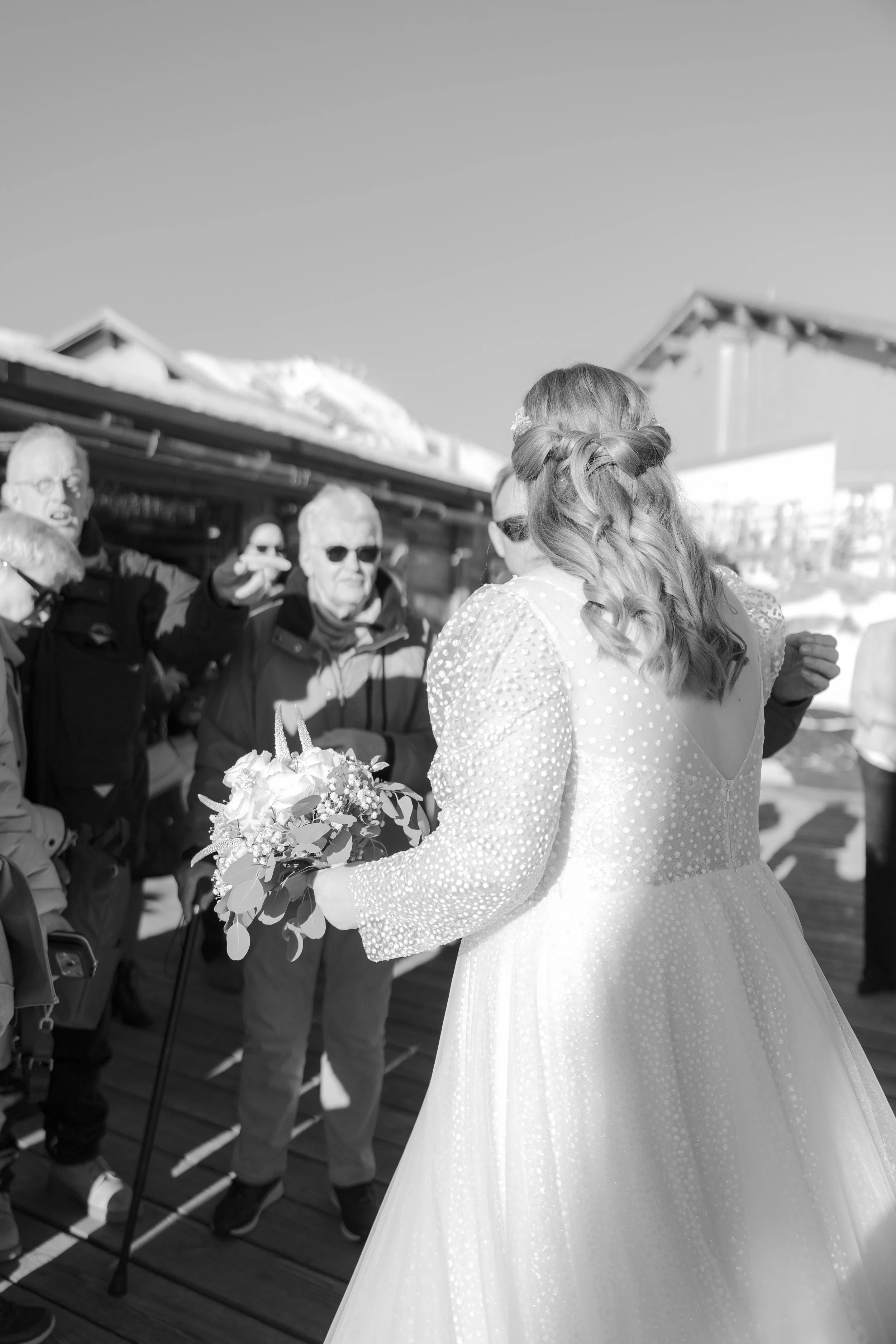 Braut mit Blumenstrauß spricht mit mehreren älteren Menschen bei einem Winterevent im Freien.