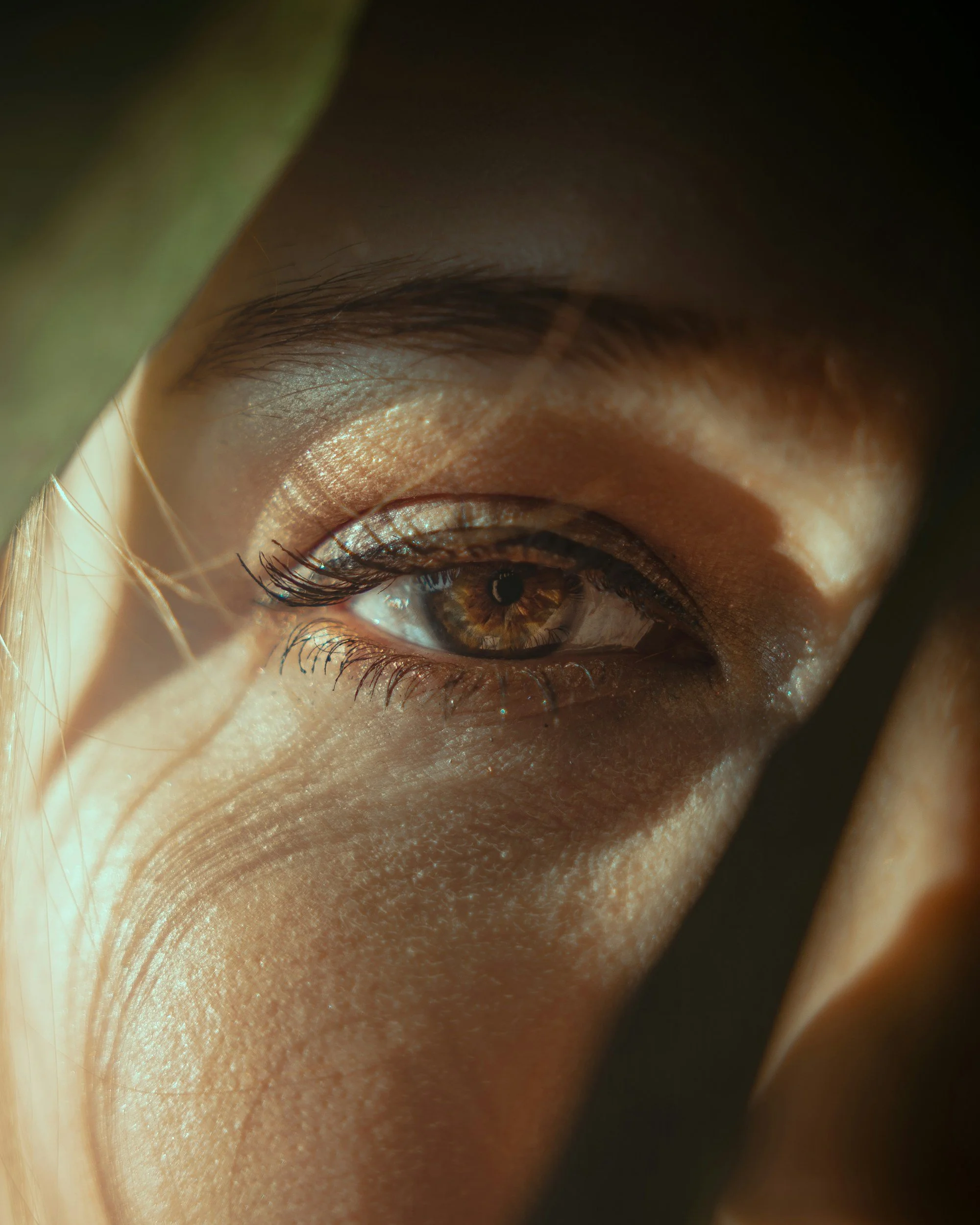 Close-up of a human eye with brown iris, eyelashes, and eyelid, partially covered by a greenish object.
