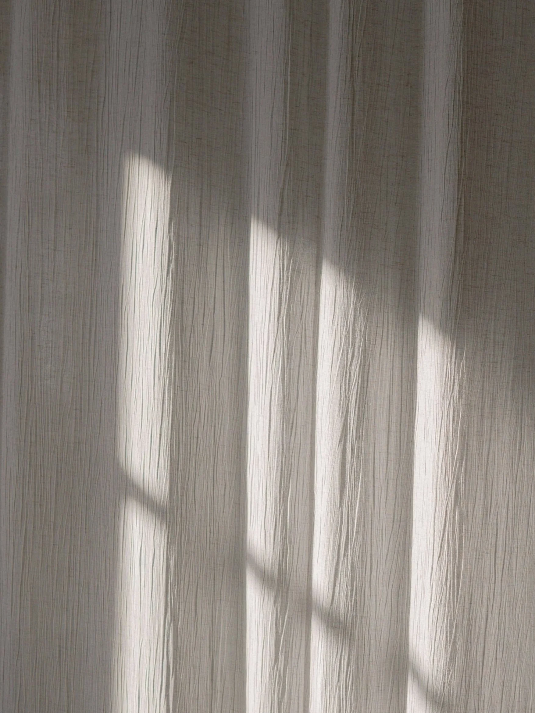 Sunlight casting shadows on a textured curtain.
