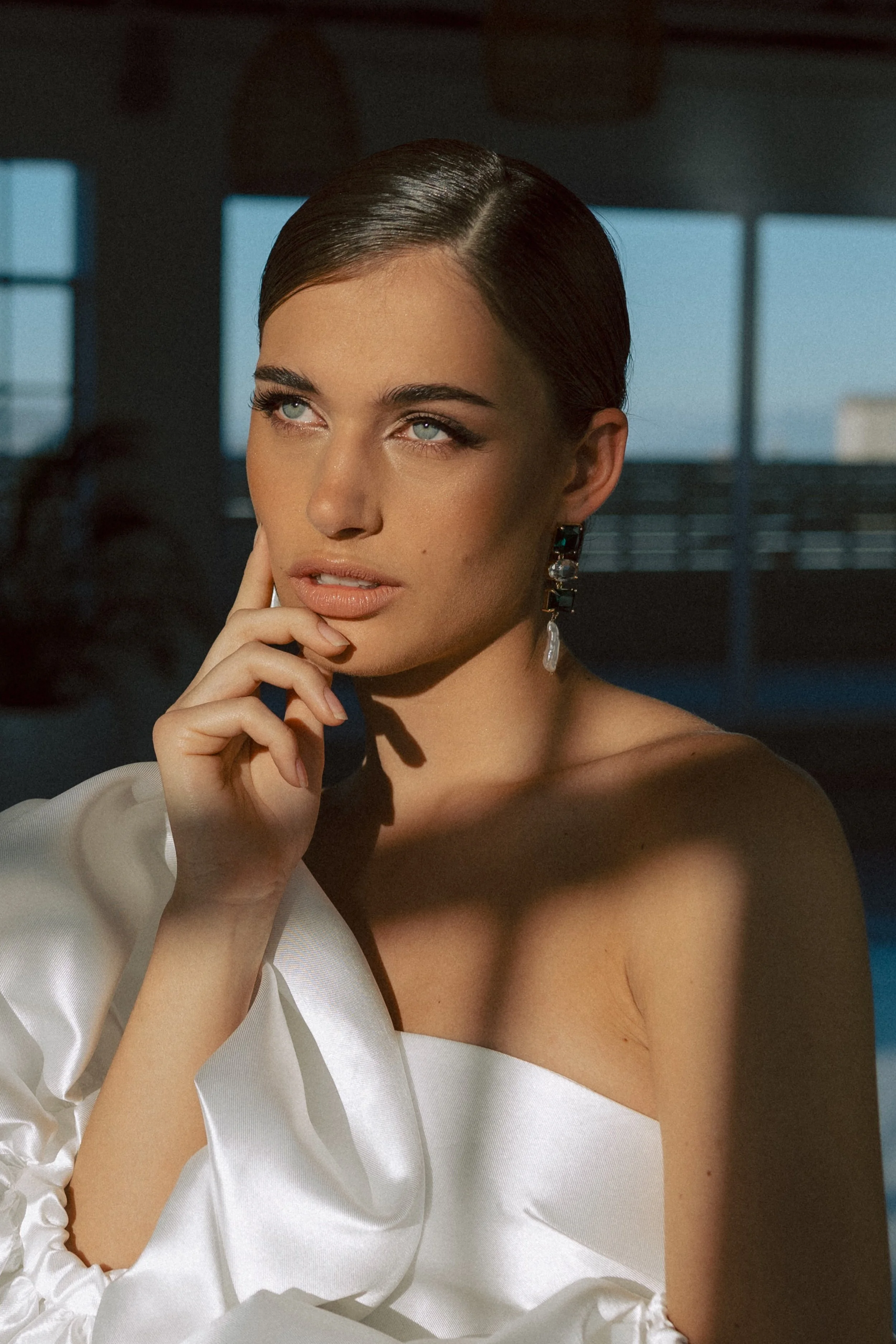 Close-up of a woman with slicked-back dark hair, Bride with a fresh, natural bridal makeup look and softly styled hair.