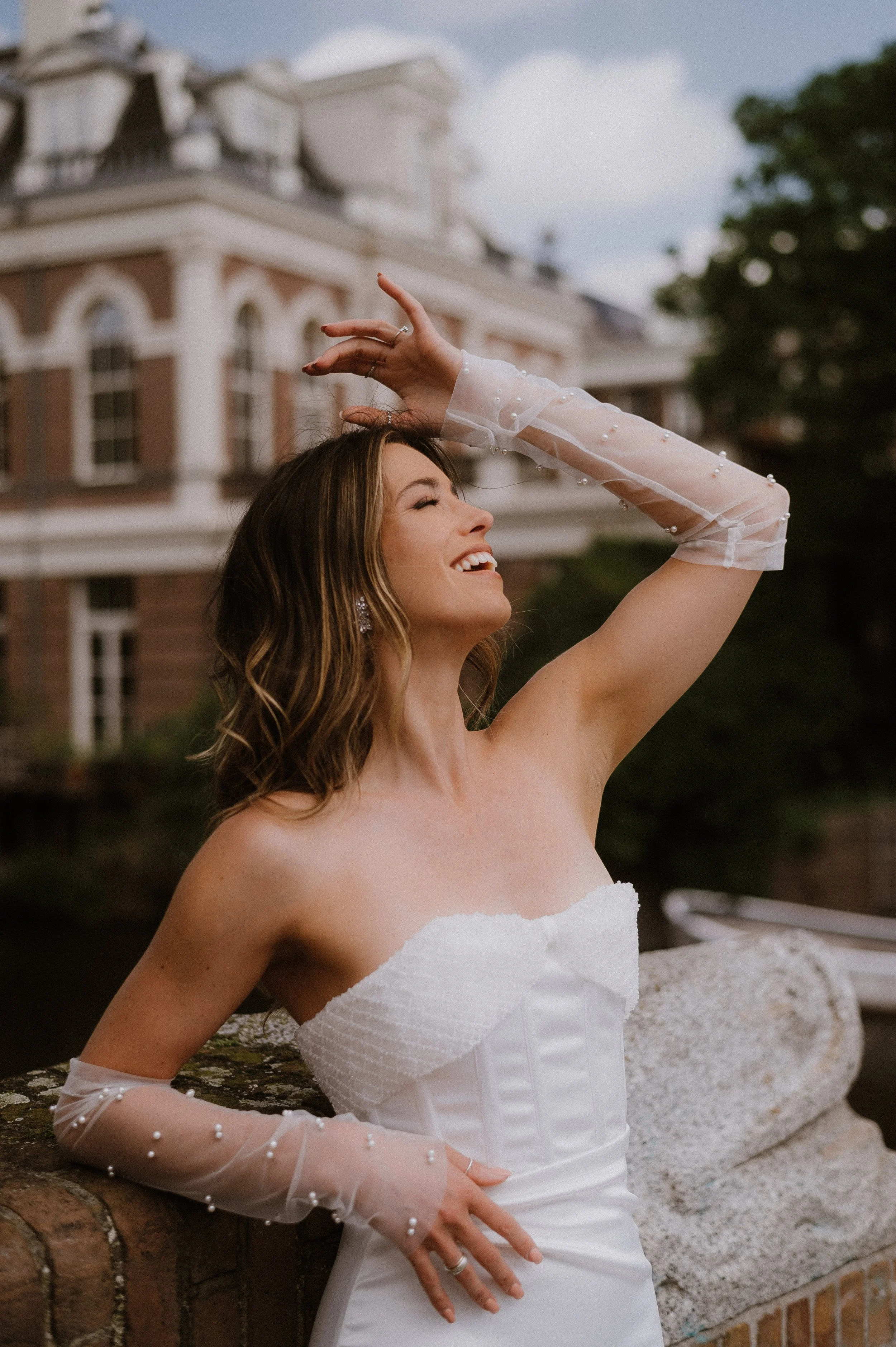 A Dutch smiling woman in a white strapless dress and sheer pearl-embellished gloves stands in Amsterdam 