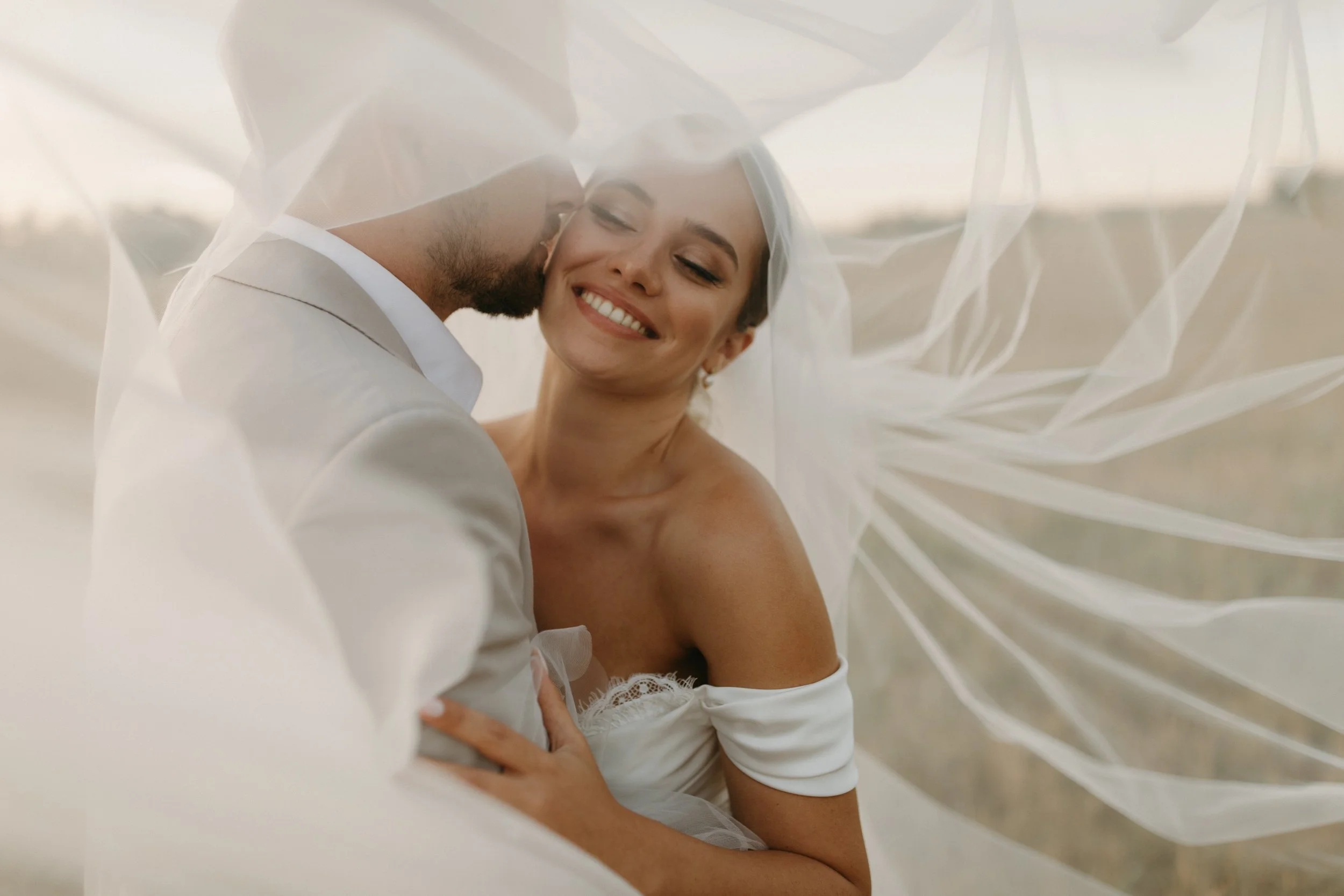 A happy bride and groom sharing an intimate moment under a white veil.