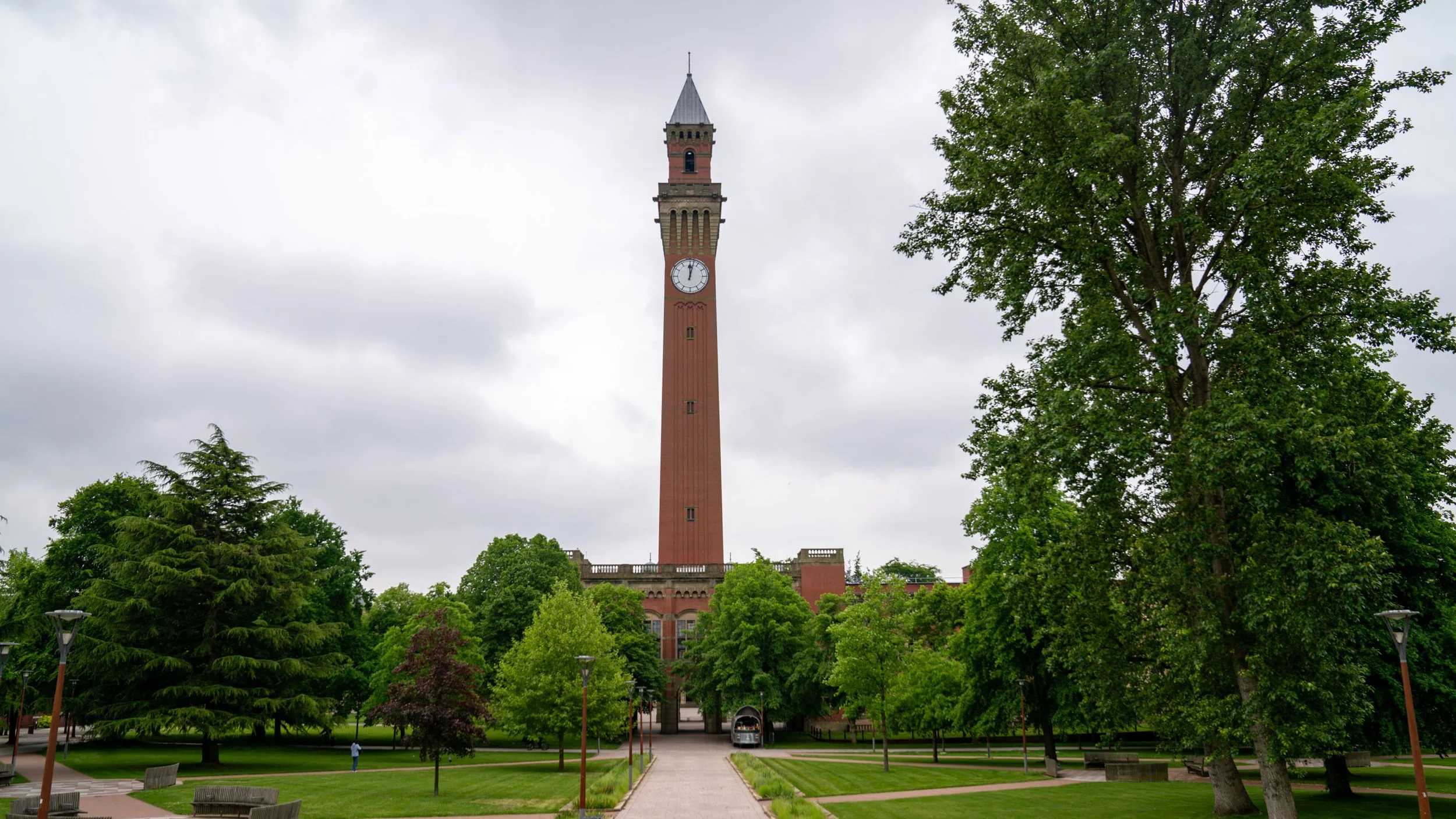 A large clock tower rises above a vibrant green park, creating a striking focal point in the landscape on University of Birmingham campus..