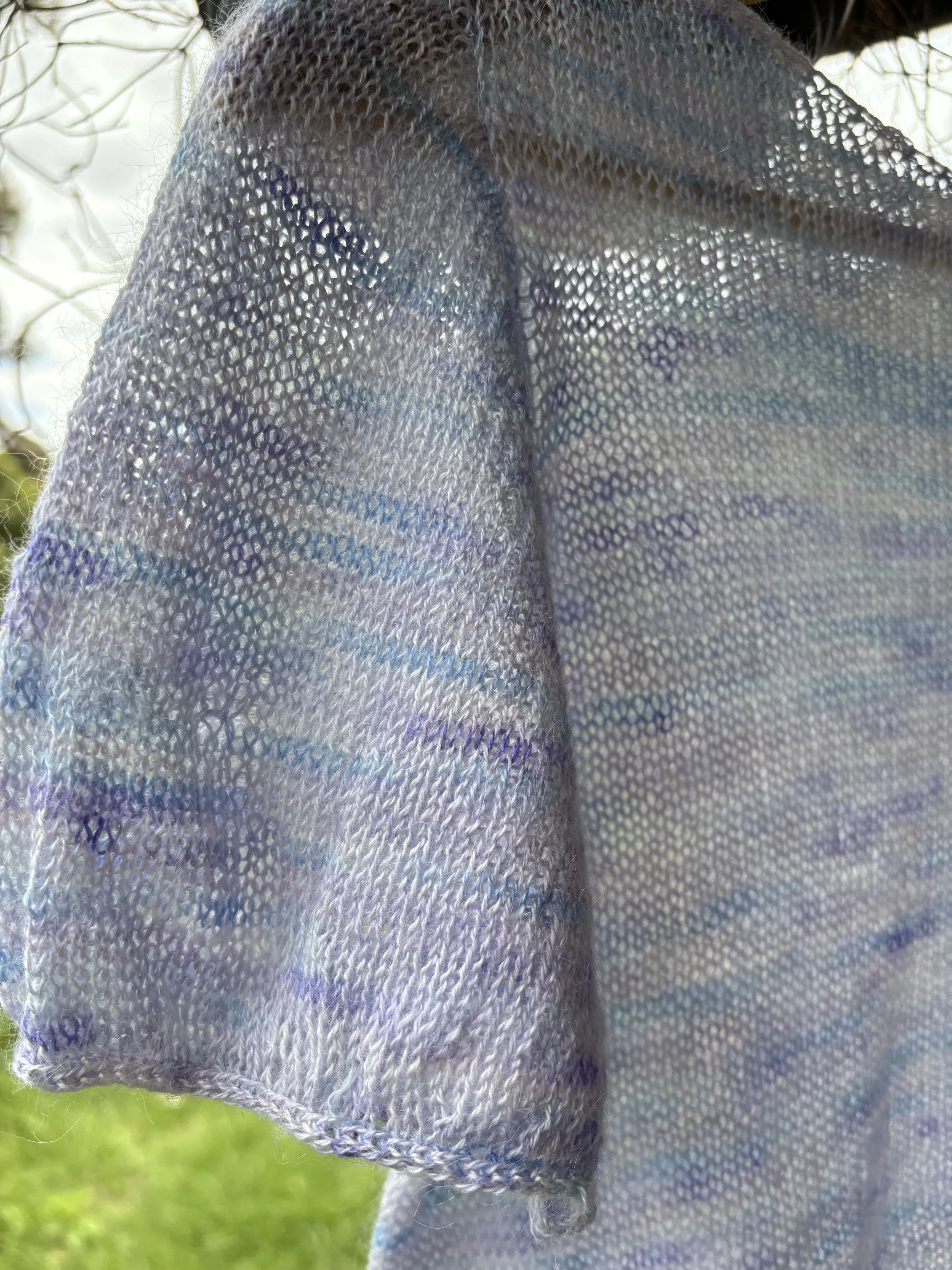Close-up of a sheer, iridescent fabric with purple and blue hues, hanging outdoors.