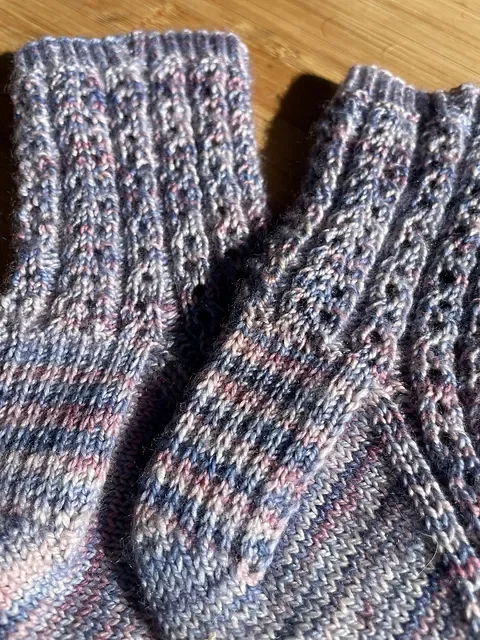 Close-up of knitted wool socks in gray, pink, and blue tones on a wooden surface.