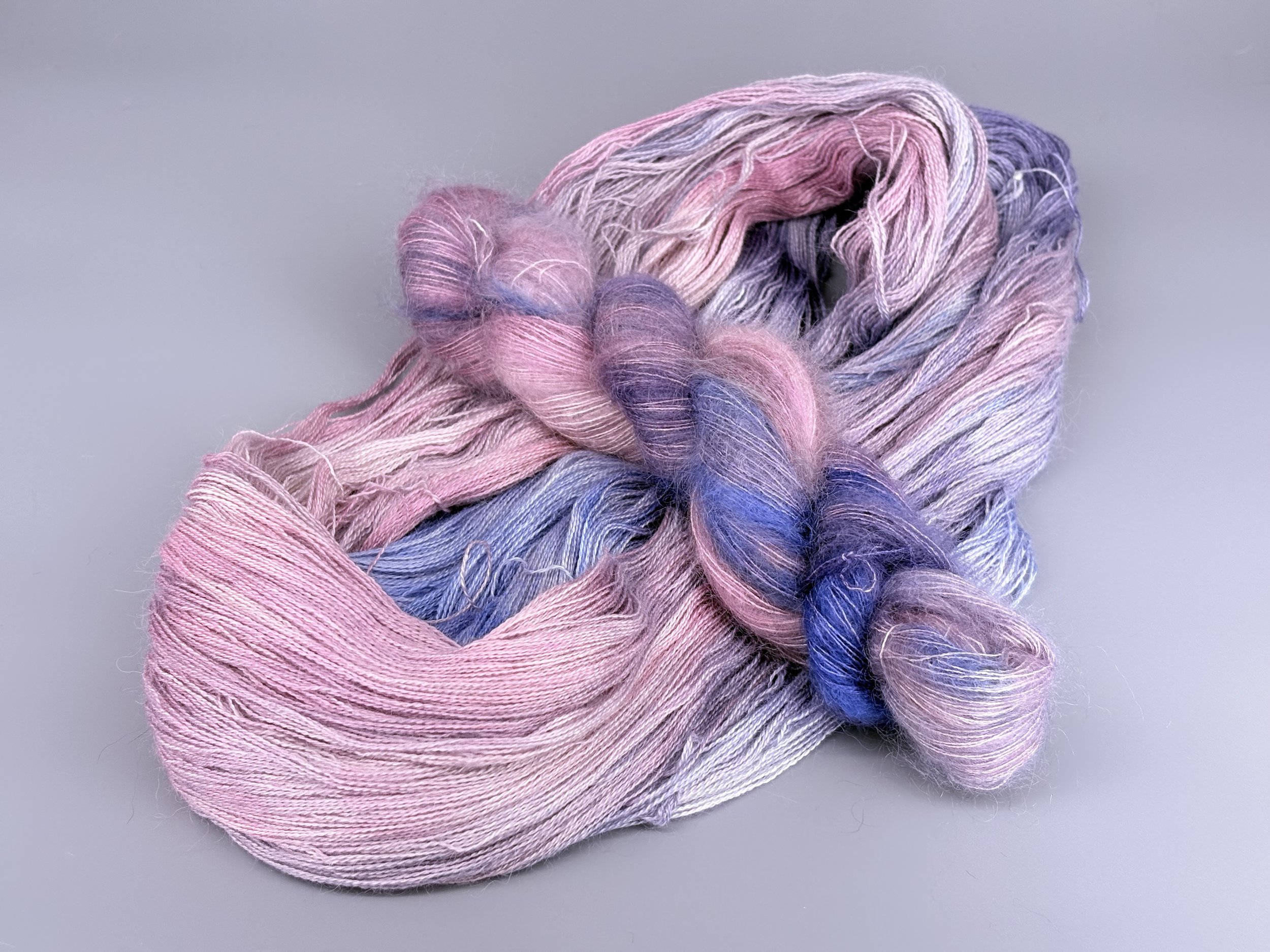 A multicolored skein of yarn in pastel shades of pink, purple, blue, and white, twisted and laid on a light gray surface.