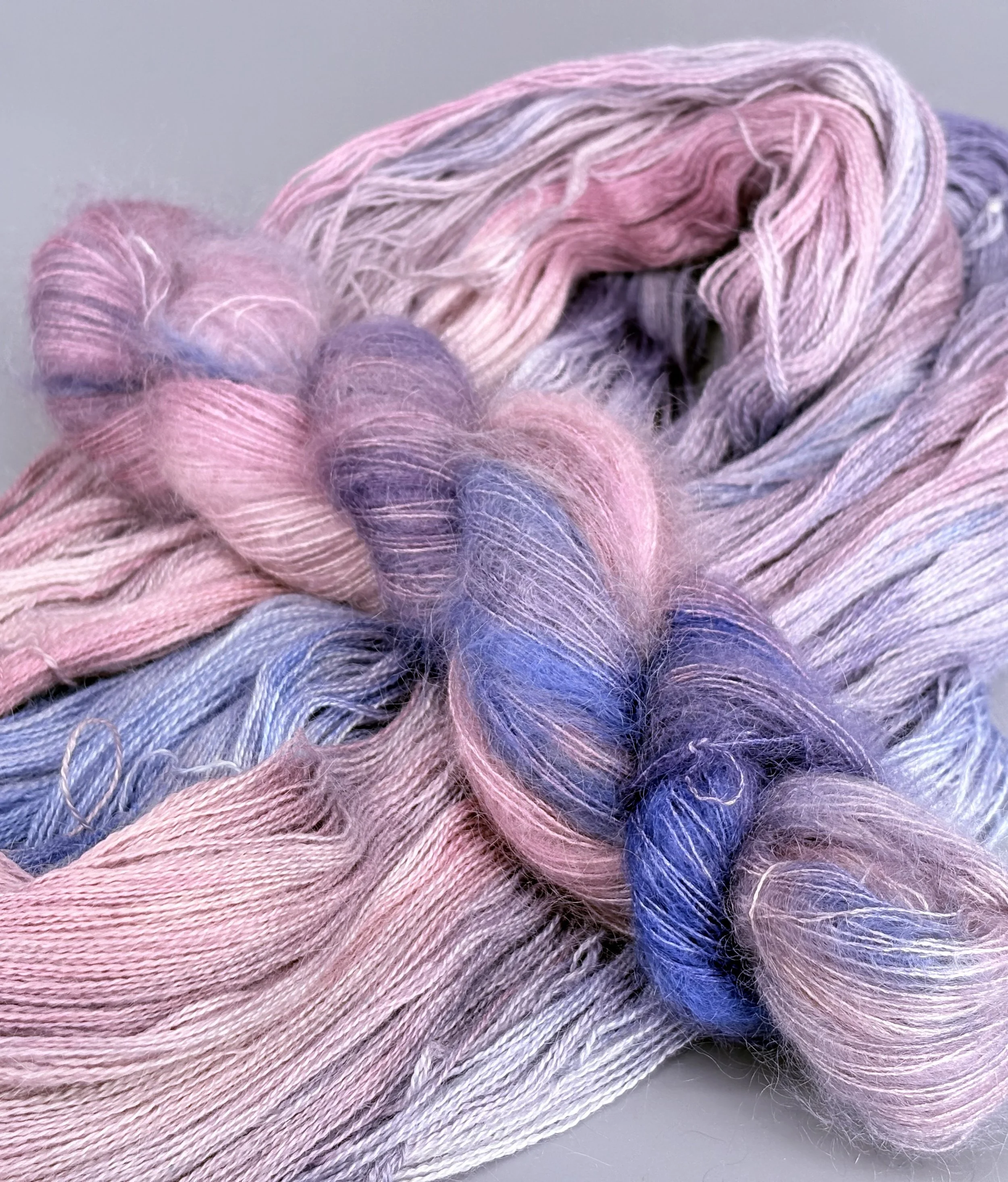 Close-up of pastel-colored yarns in shades of pink, purple, and blue, with some of the yarns braided and others loose.