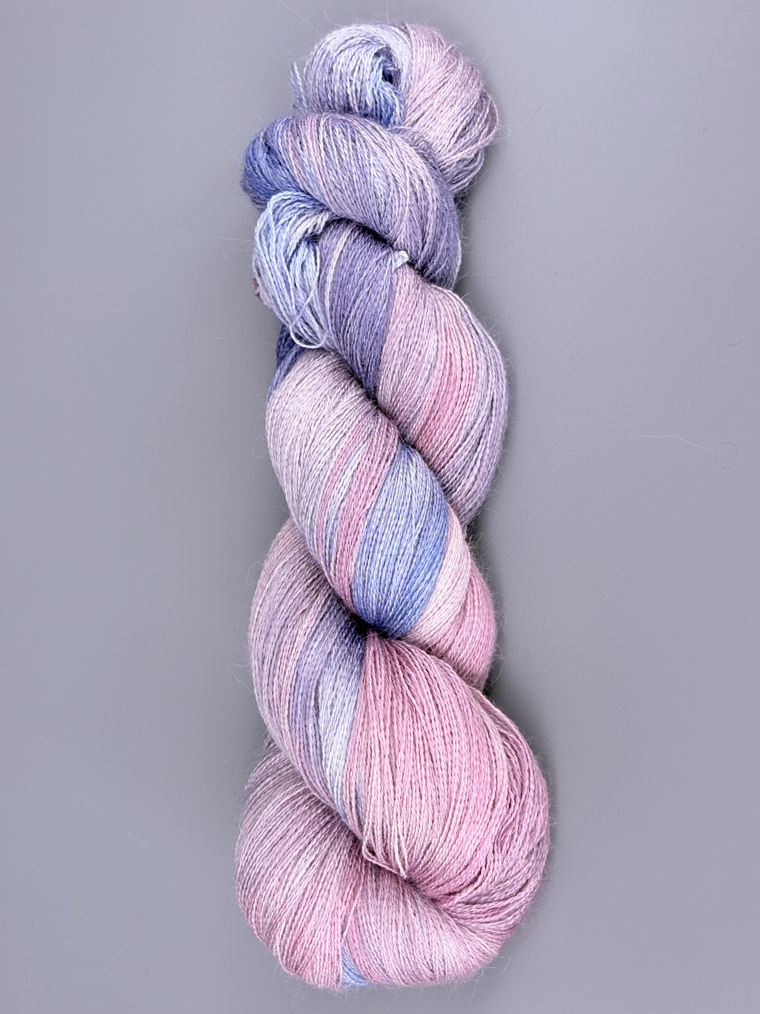 A skein of pastel-colored yarn twisted into a hank, featuring shades of pink, purple, and blue, against a gray background.