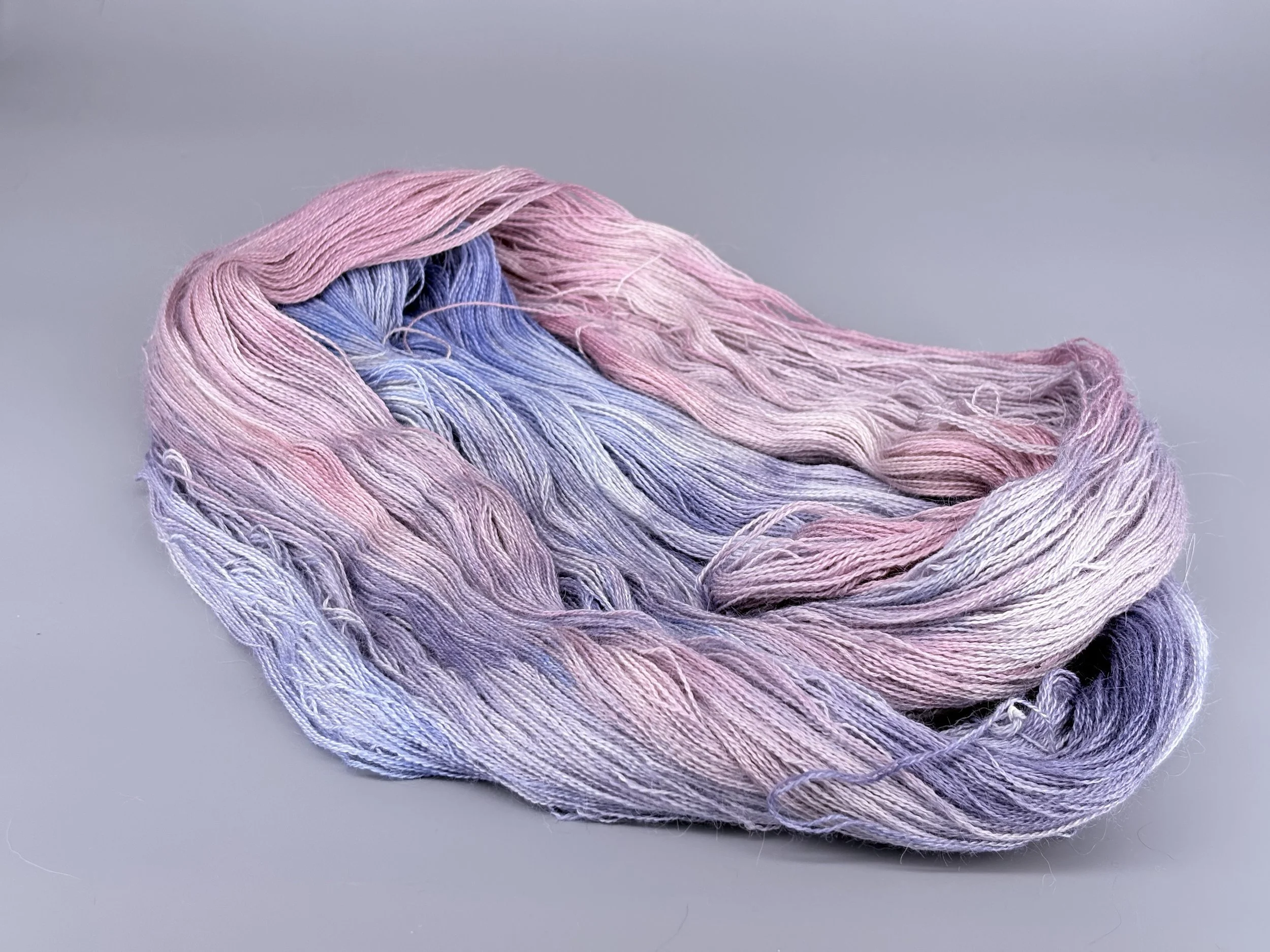 A skein of multicolored pastel yarn, predominantly pink, purple, and blue, laid on a gray surface.