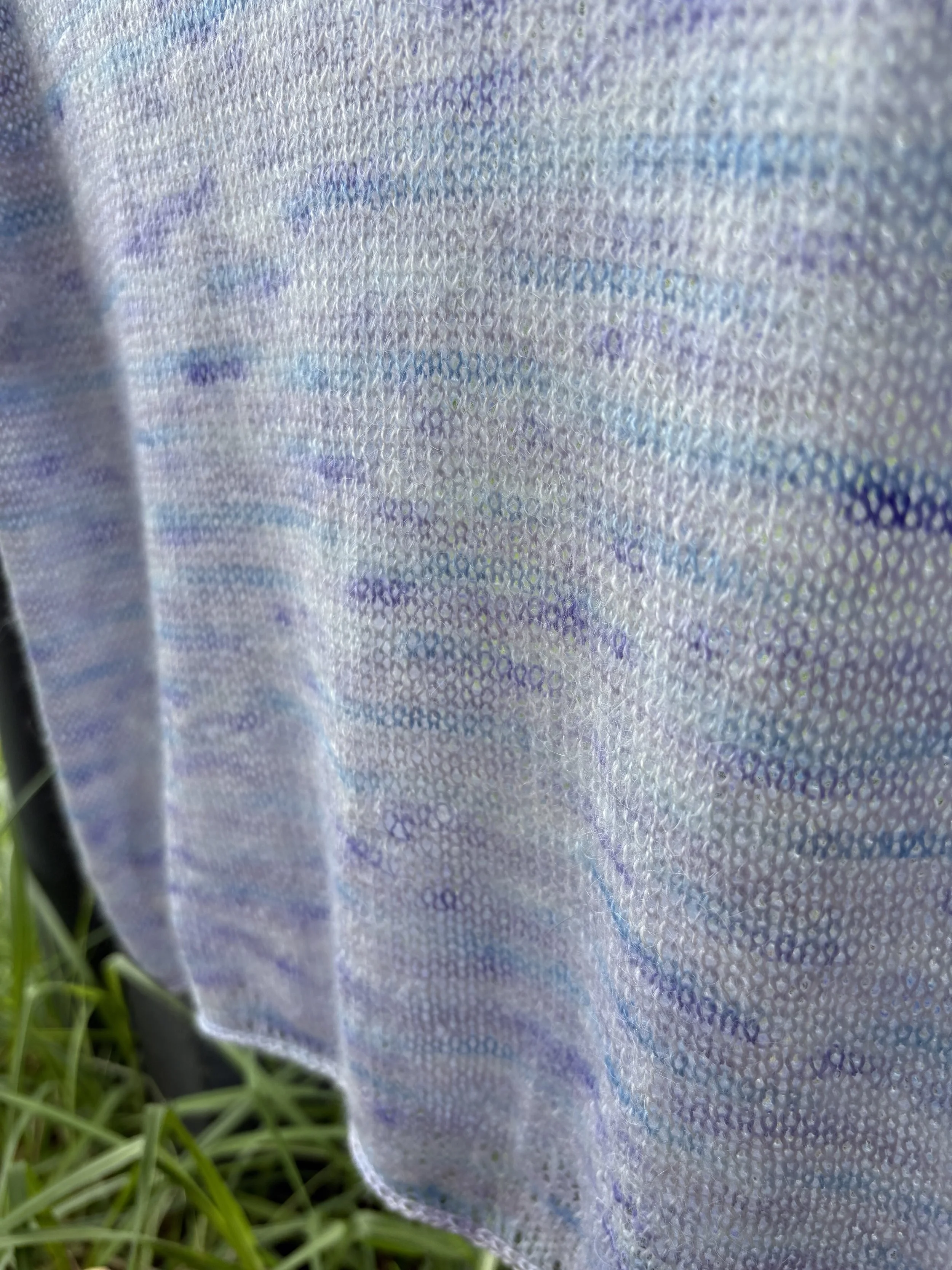 Close-up of a fabric with iridescent surface reflecting various colors, with some grass visible at the bottom.