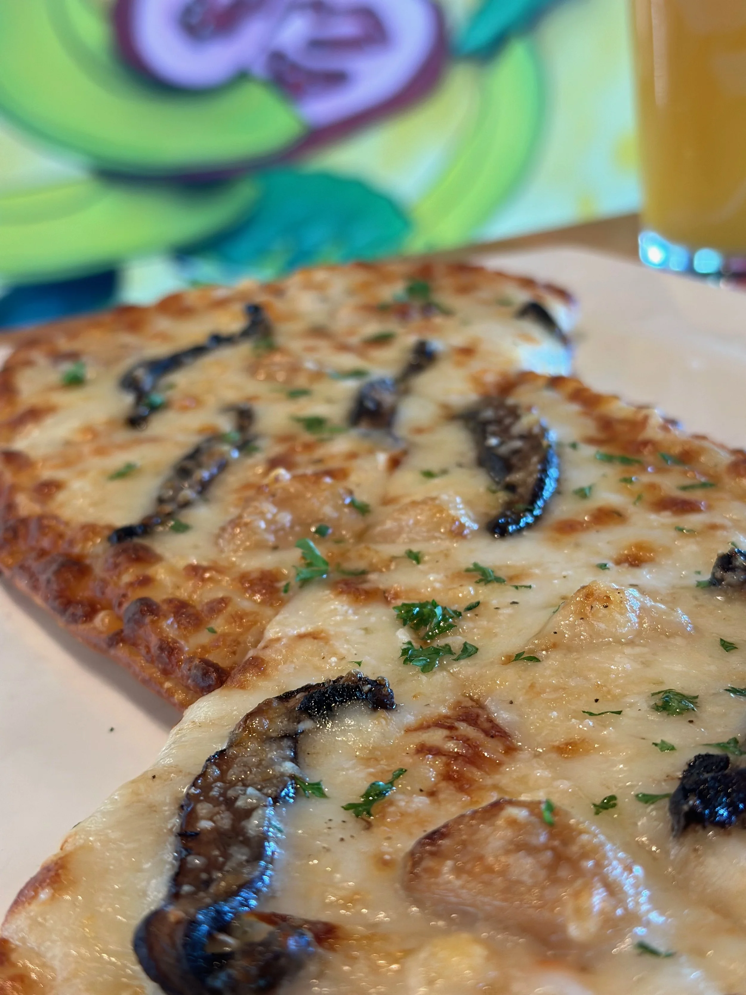 Slice of mushroom and cheese pizza on a plate with a glass of beer in the background.