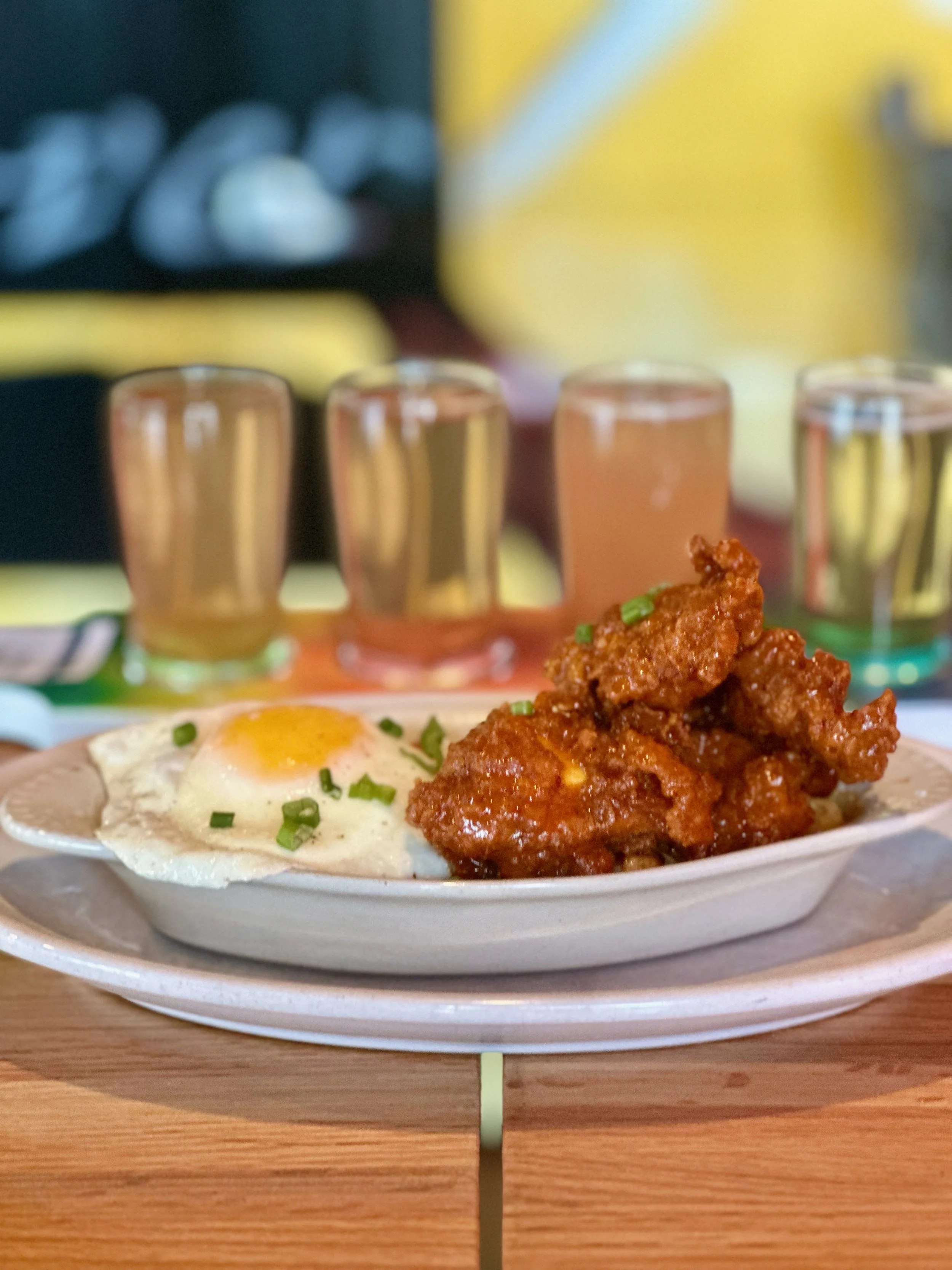 Plate with fried chicken and a fried egg, garnished with chopped green onions, on a wooden table.