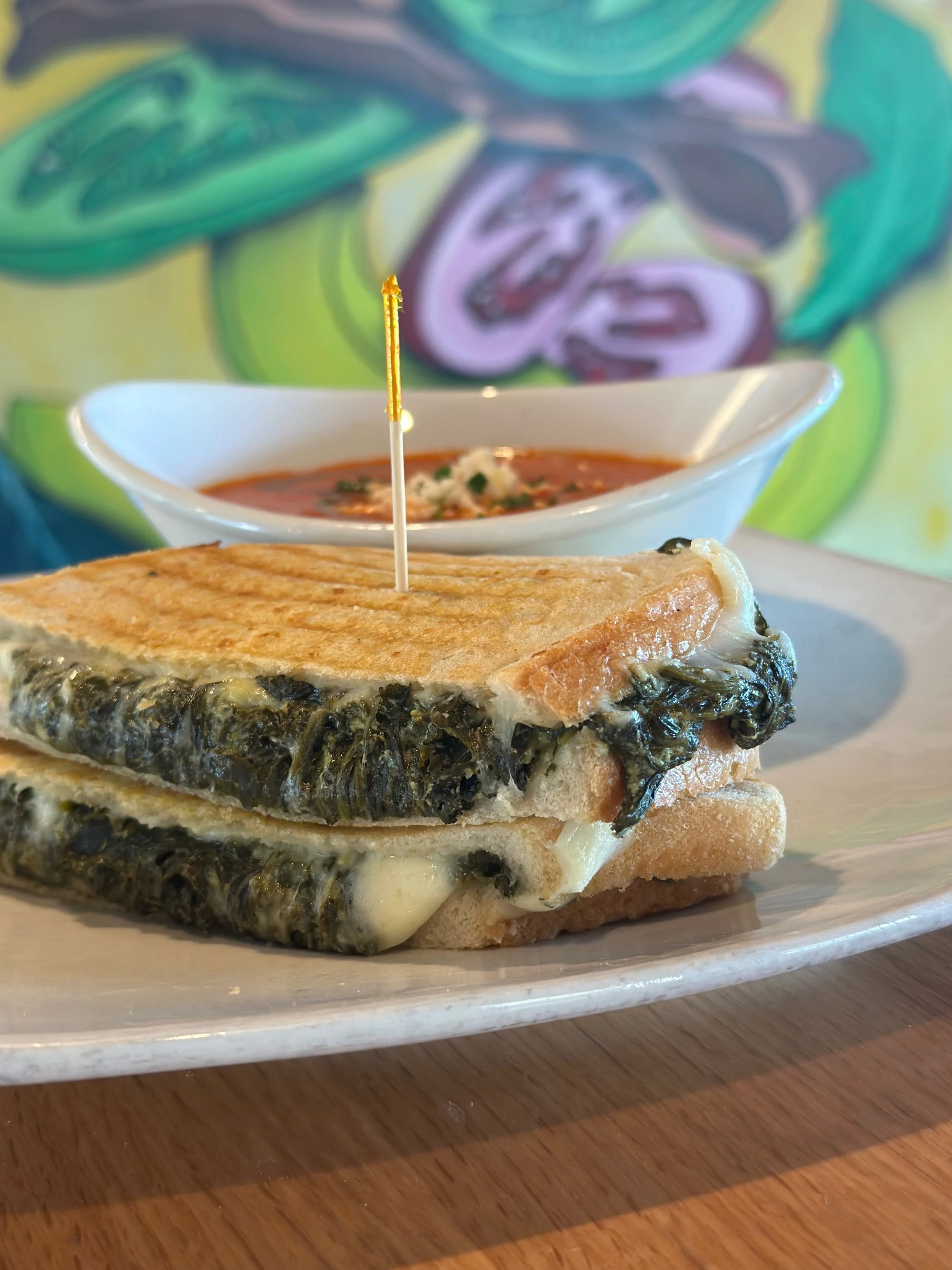 Spinach and cheese grilled sandwich with tomato soup in the background.