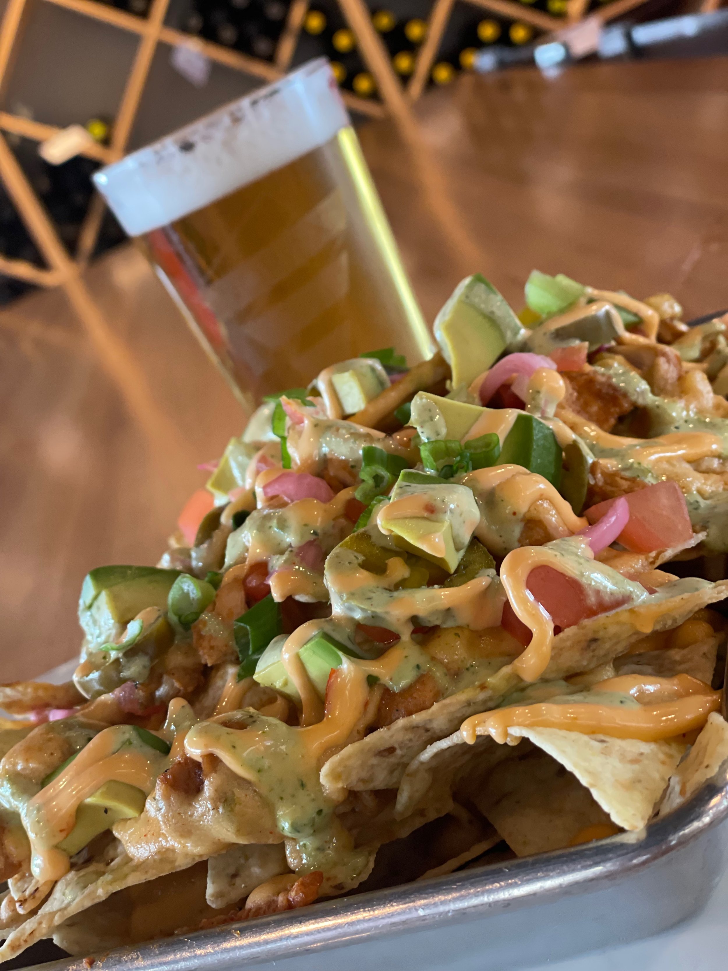 Close-up of loaded nachos with cheese, vegetables, and a side of beer in a glass.