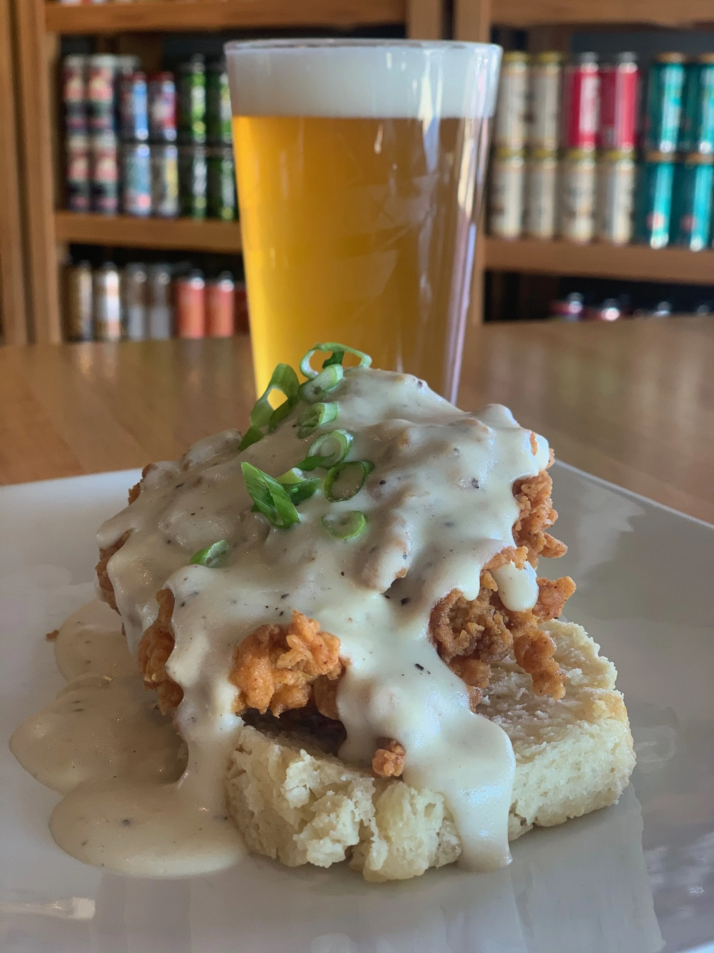 Fried chicken and gravy on a biscuit with chopped green onions, served with a glass of beer.