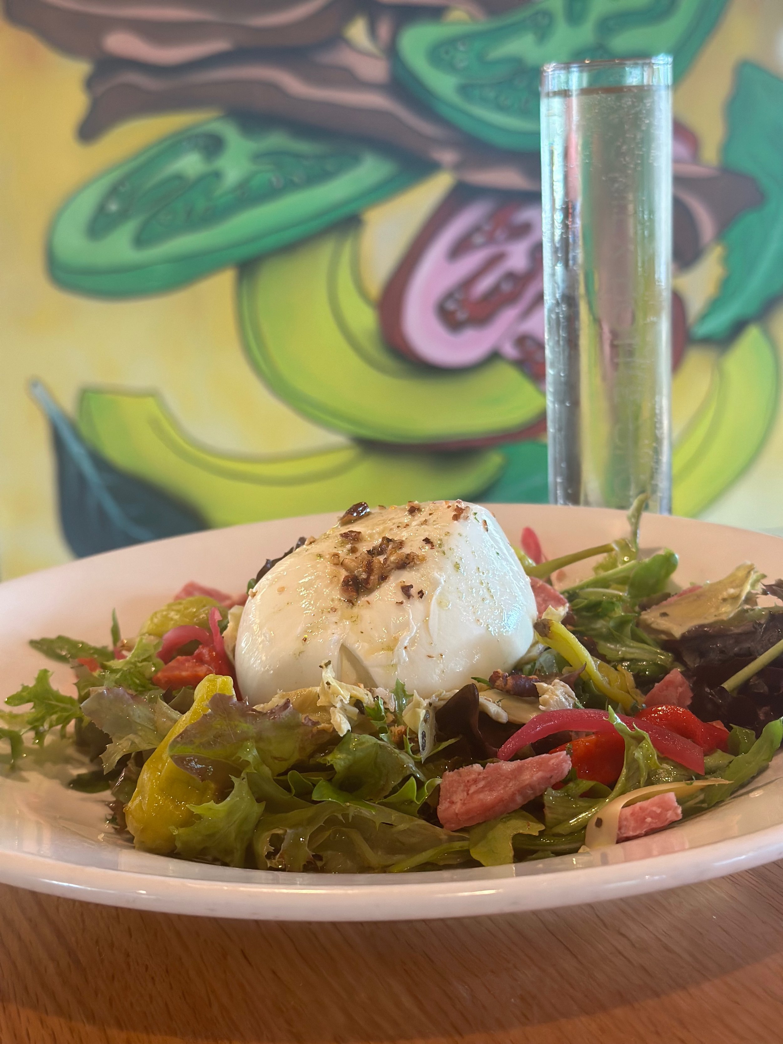 Salad with mixed greens, tomatoes, and slices of pink meat, topped with a poached egg and sprinkled with black pepper, served on a white plate.
