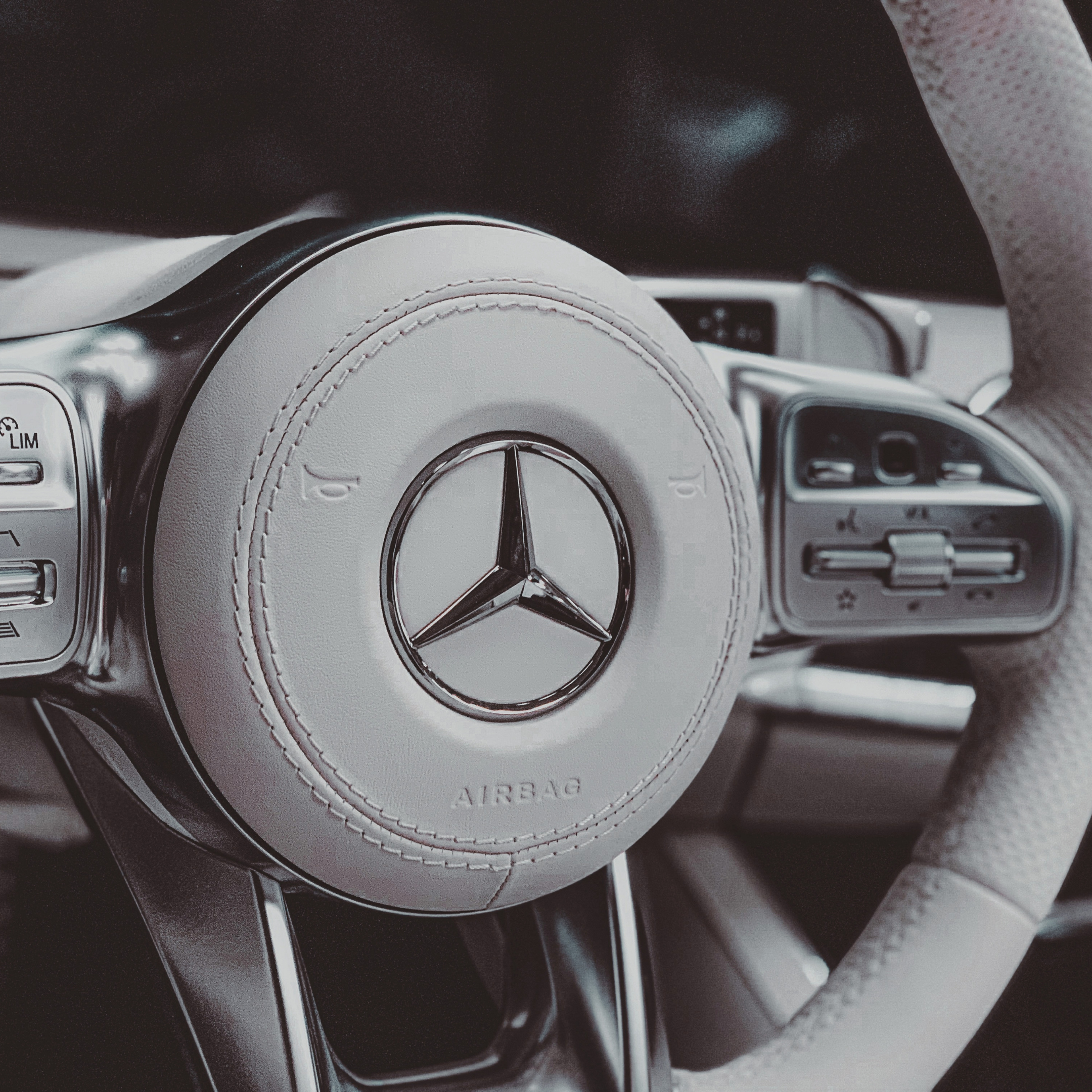 Close-up of a Mercedes-Benz steering wheel with white leather and chrome accents inside a car.