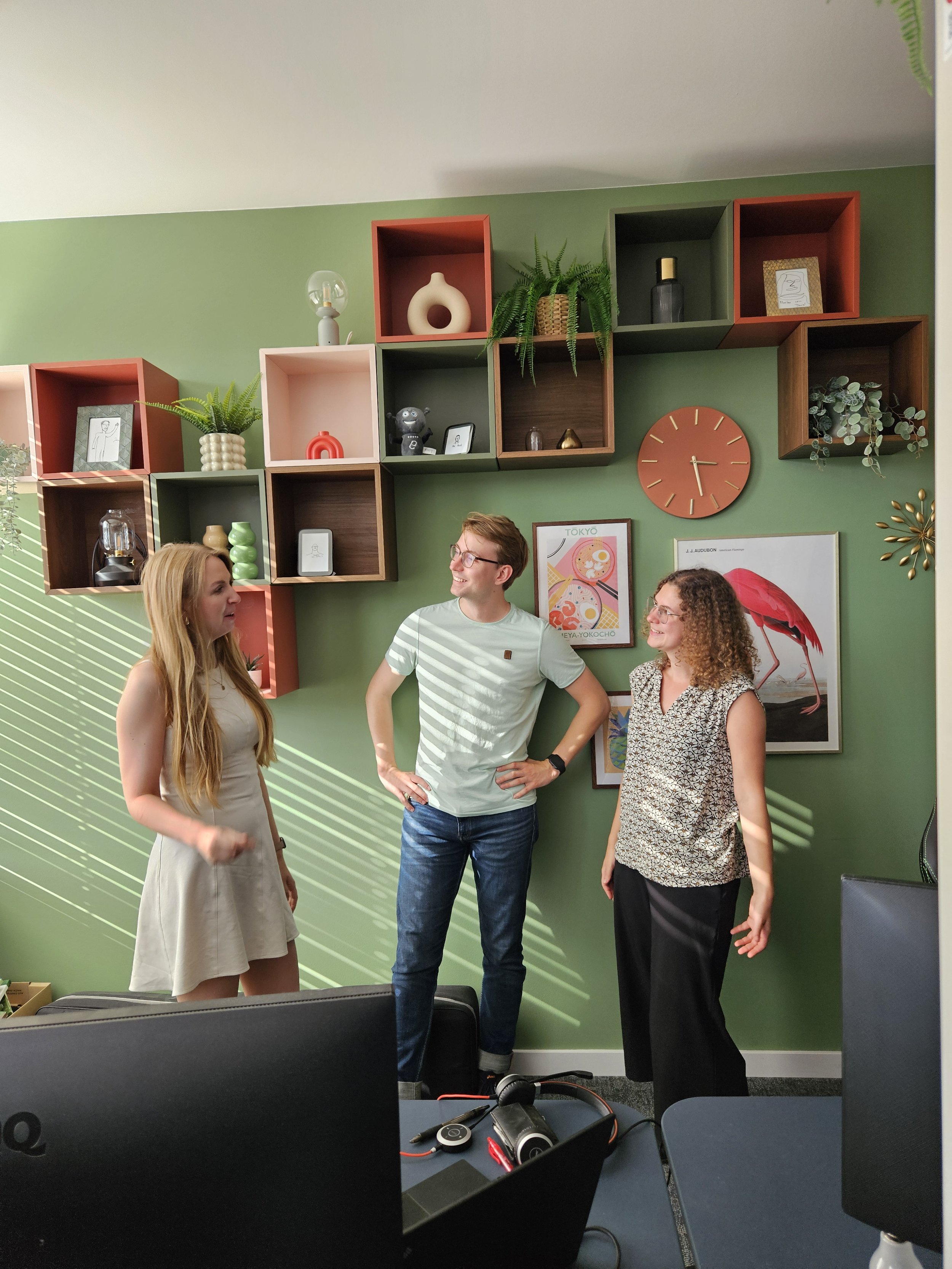 Drei Leute stehen zusammen im Büro und unterhalten sich.