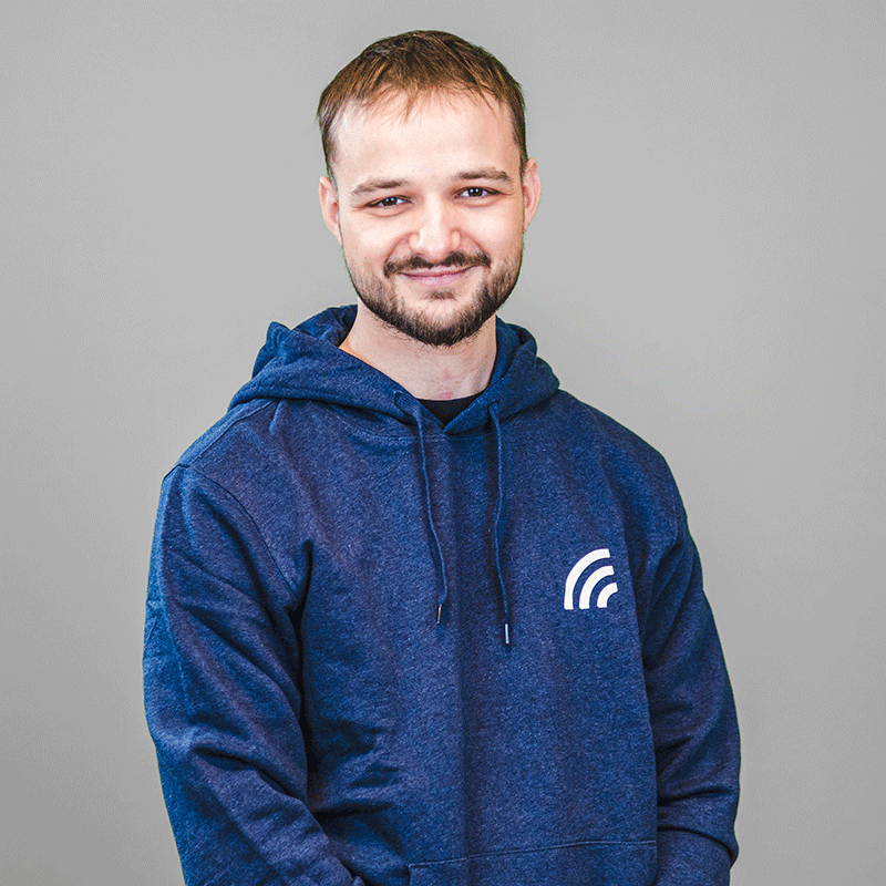 Eduard Lorer trägt blauen Hoodie mit dem Logo von Hochfrequenz und steht vor einem grauen Hintergrund.