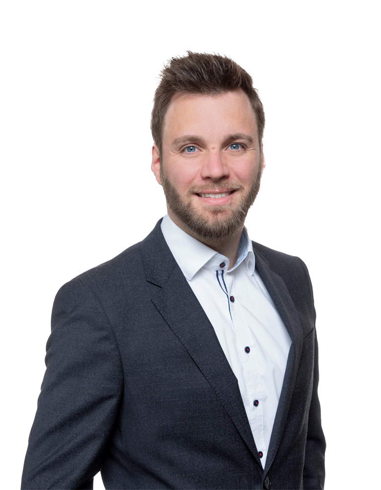 Ein junger Mann in formeller Kleidung, trägt einen dunklen Anzug und ein weißes Hemd, lächelt freundlich.