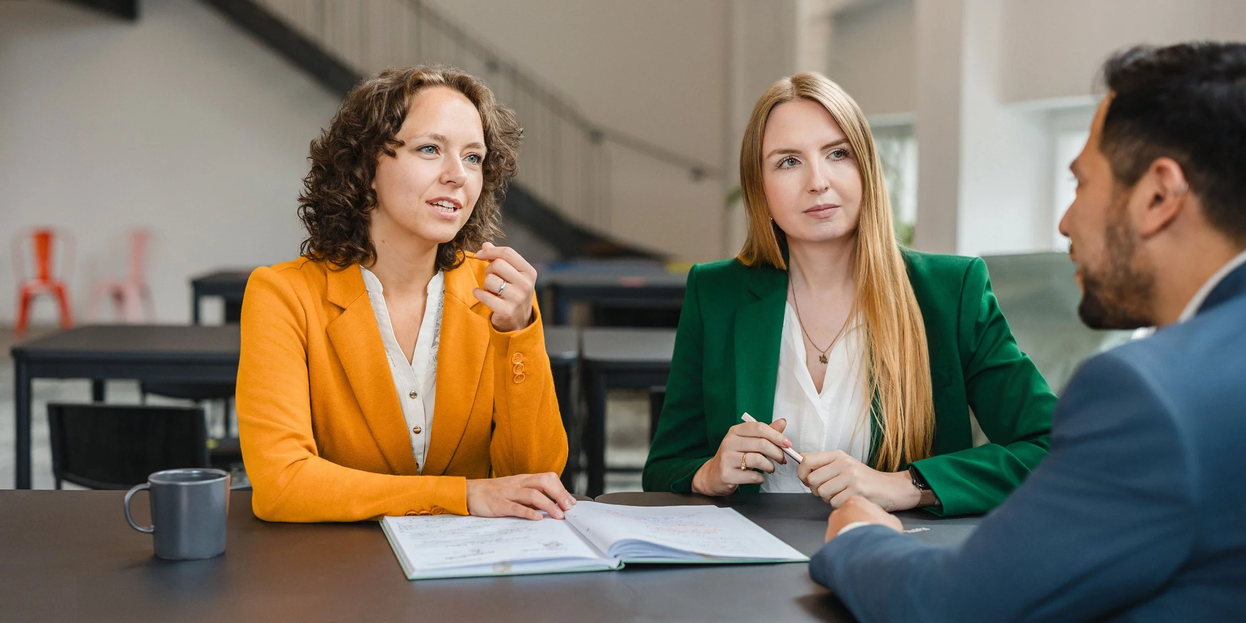Drei Menschen im Gespräch bei einem Meeting, zwei Frauen und ein Mann, sitzen an einem Tisch. Sie unterhalten sich über Prozesse in der Energiewirtschaft.