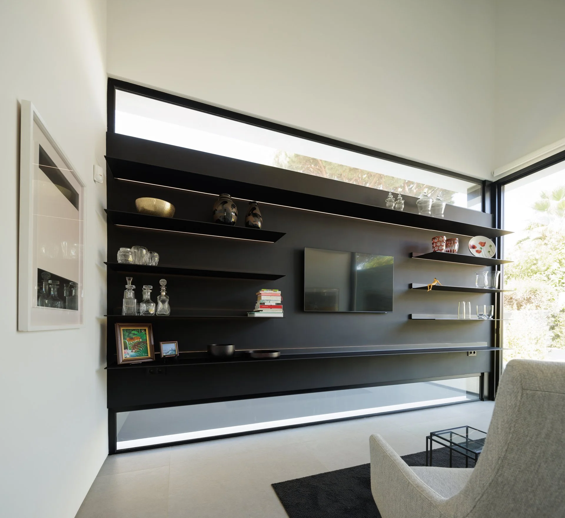 Bespoke black TV cabinet by A+ Interiors with shelving and a grey armchair facing the television 