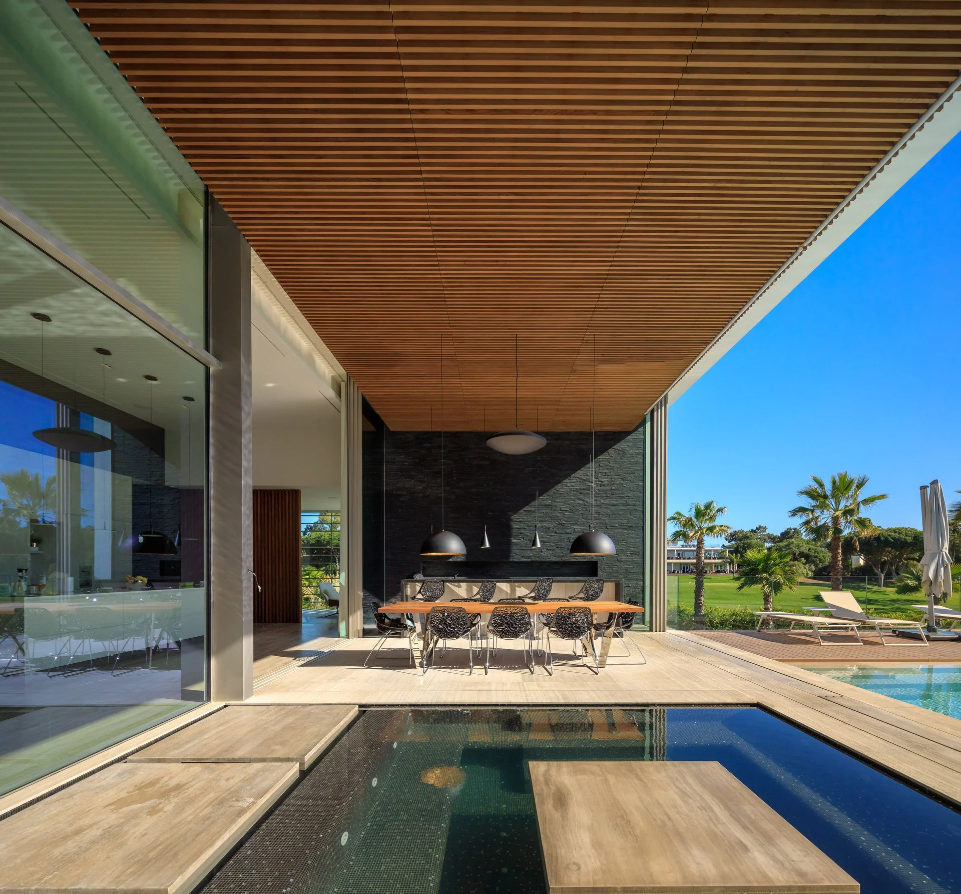 Outdoor dining project by A+ Interiors, with a stunning dining table, chairs and outdoor kitchen next to a modern jacuzzi designed by Vasco Vieira Arquitectos