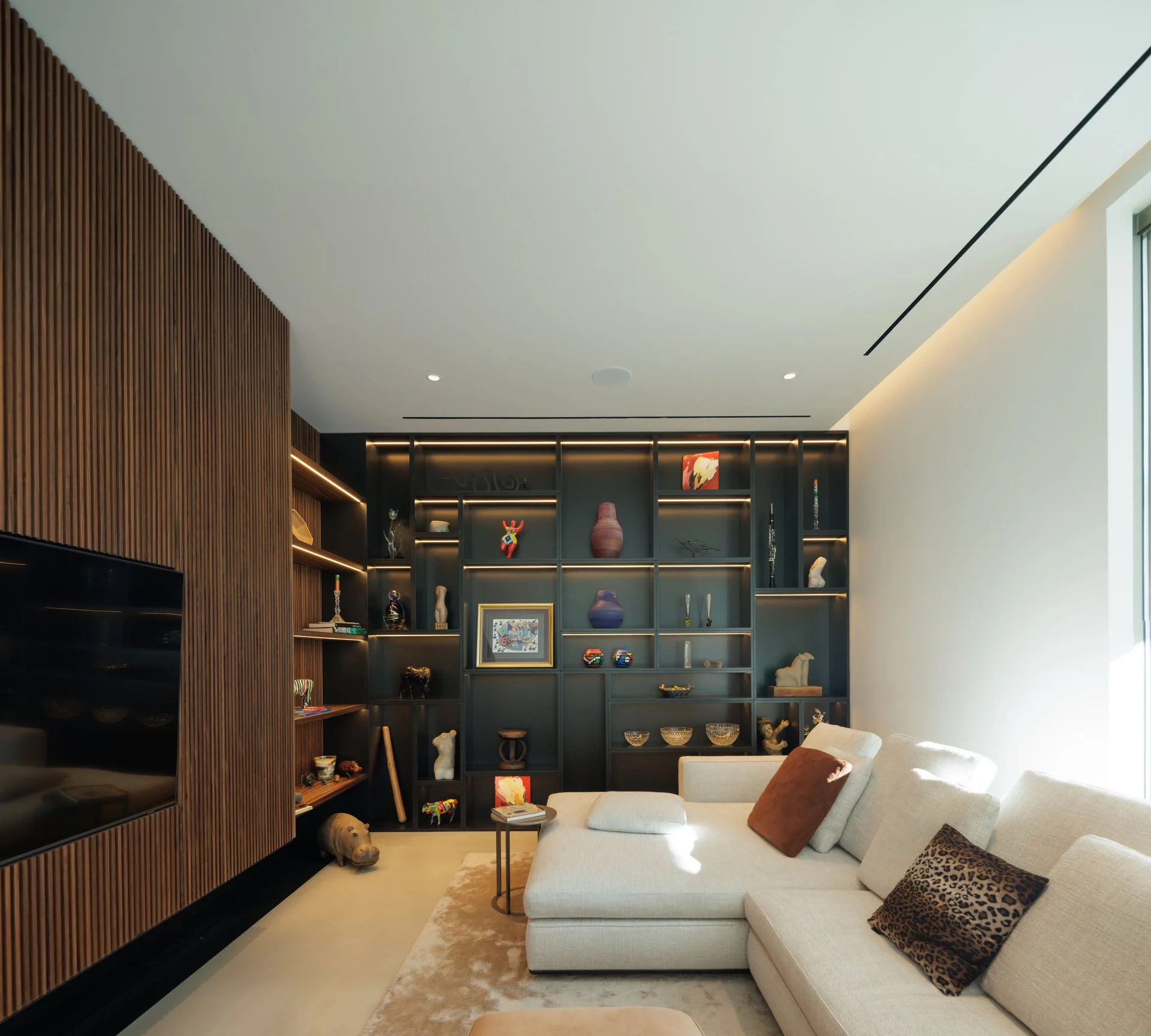 Cozy TV nook with wood panelling, a white sofa and impressive black bespoke cabinet by A+ Interiors