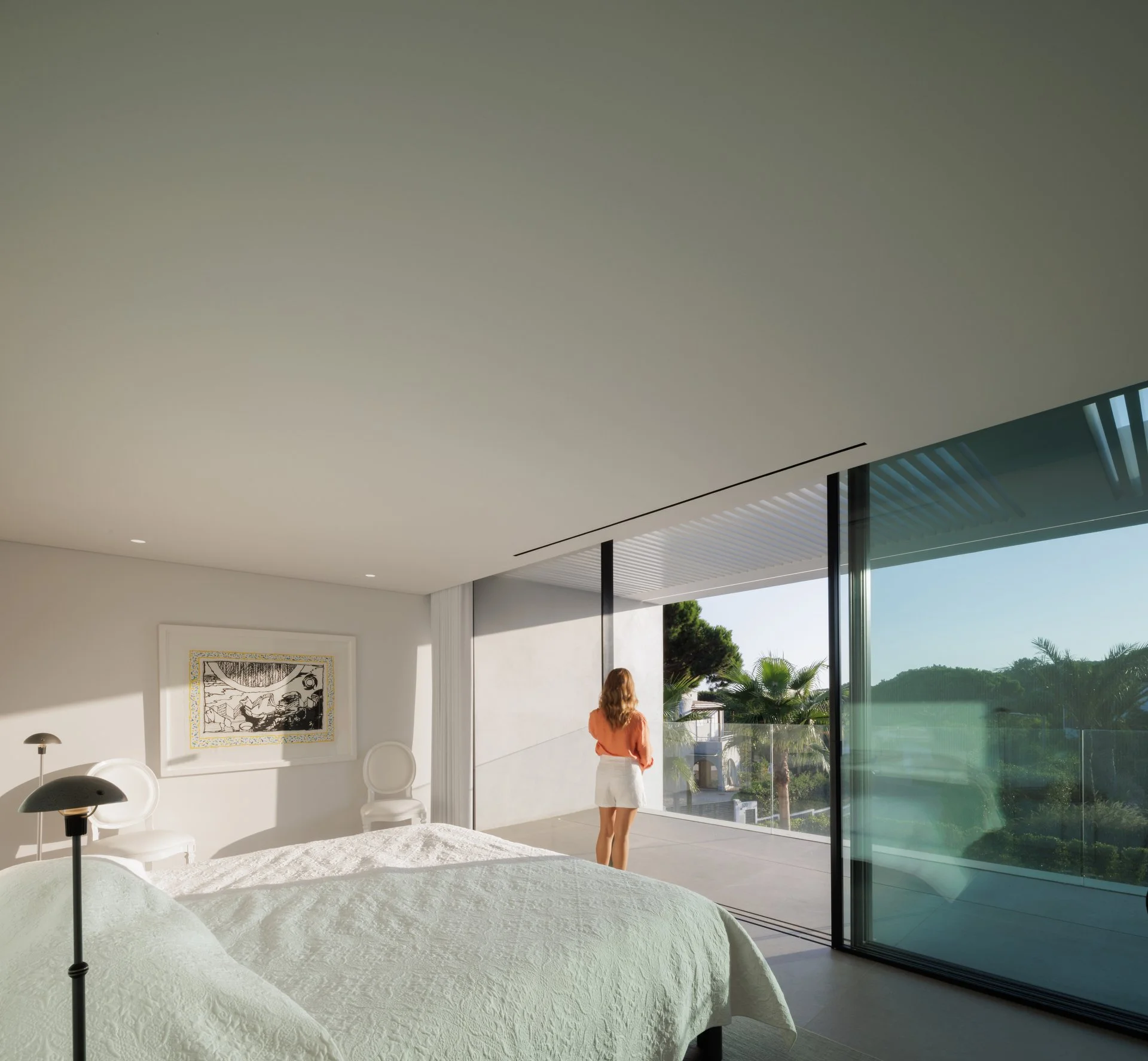 Clean, white bedroom with a king-sized bed, statement art piece on the wall and beautiful natural lighting