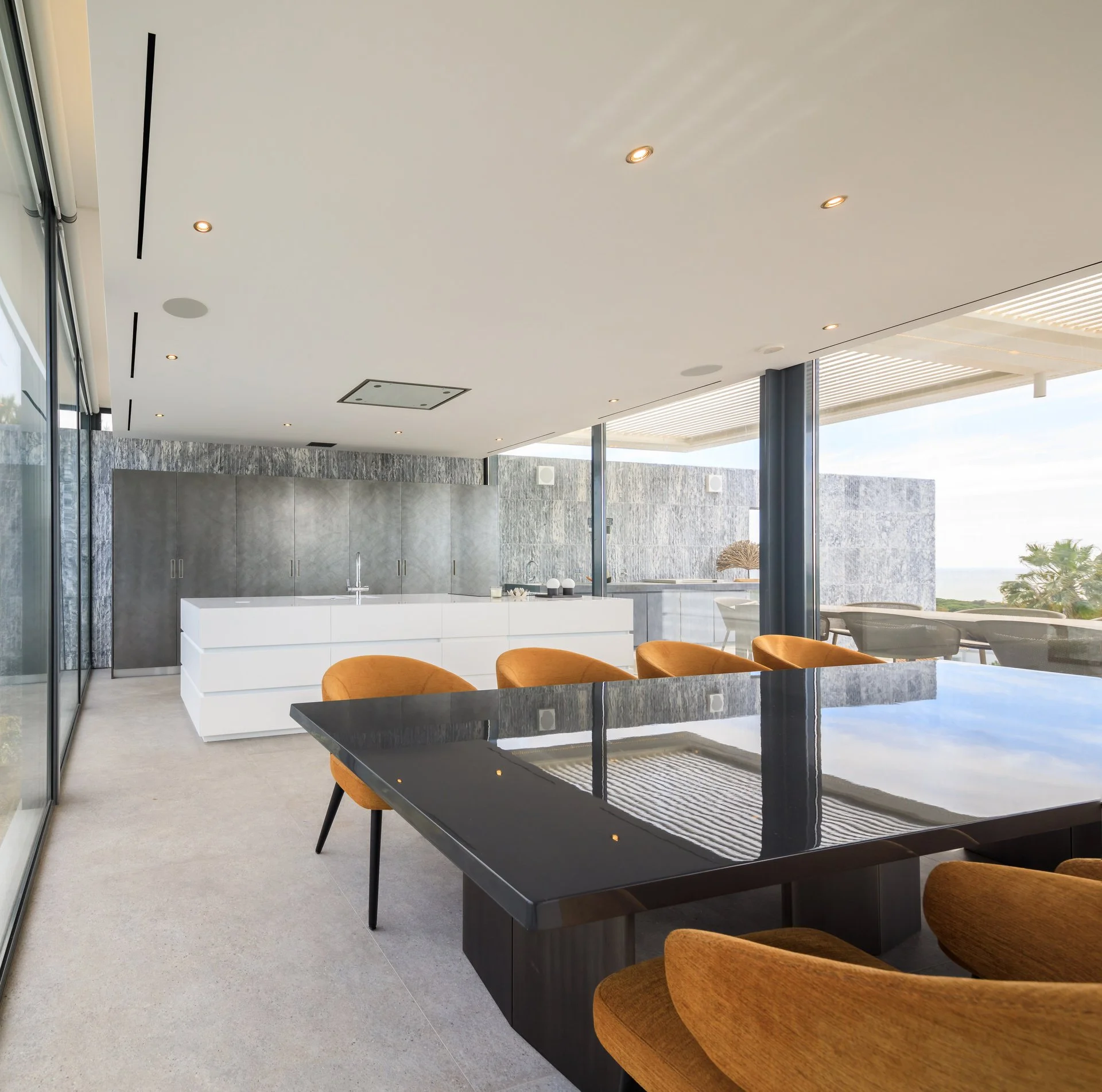 Beautiful dining room project with full length windows on either side, a statement black dining table with eight orange dining chairs, and a white show kitchen in the background