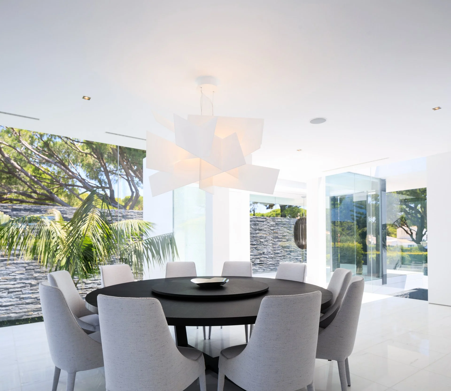 Luxury open-plan dining space with a round black table and grey dining chairs and a statement lighting feature
