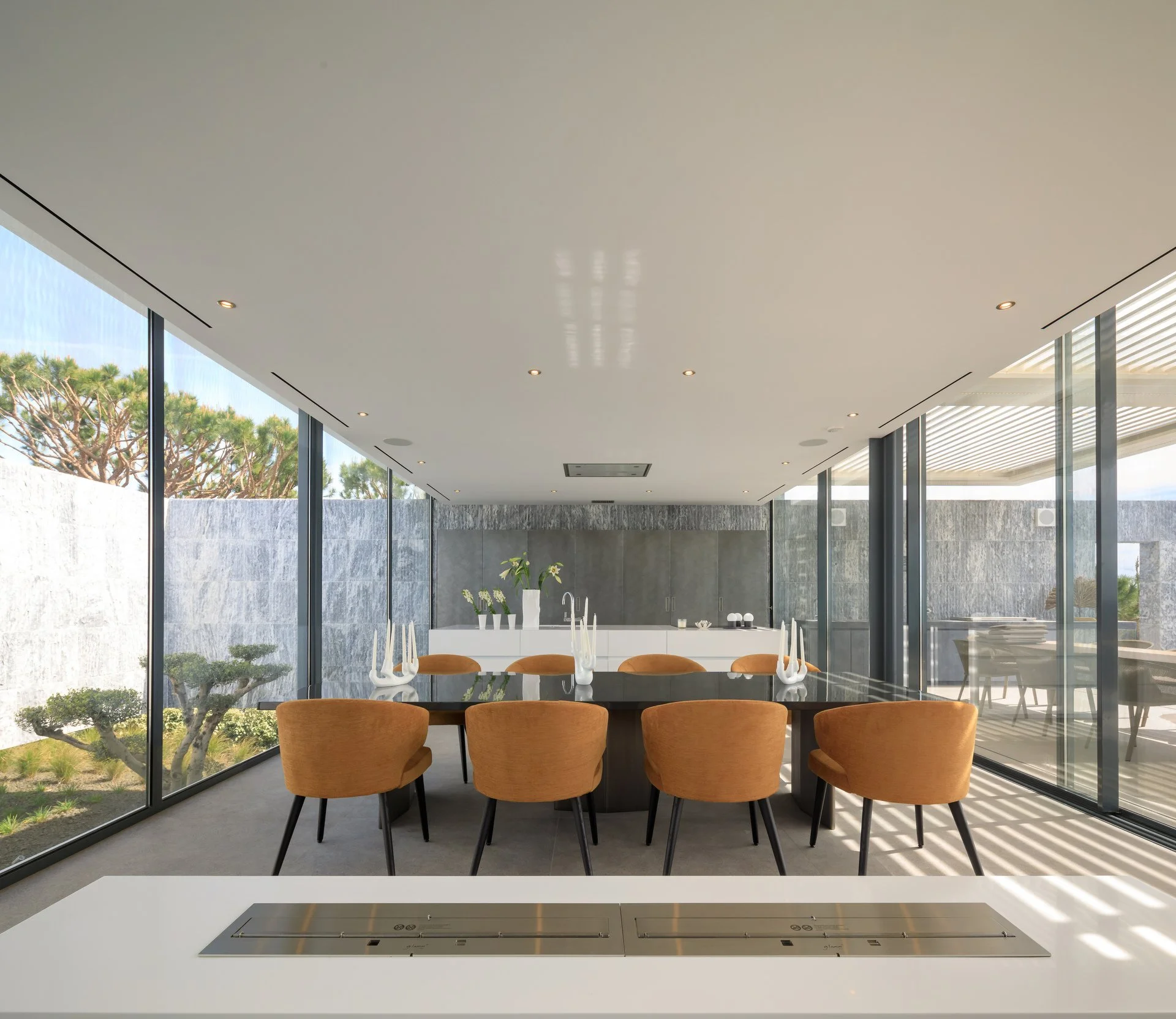 Beautiful dining room project with full length windows on either side, a statement black dining table with eight orange dining chairs, a white show kitchen in the background and an ethanol fireplace in the forefront