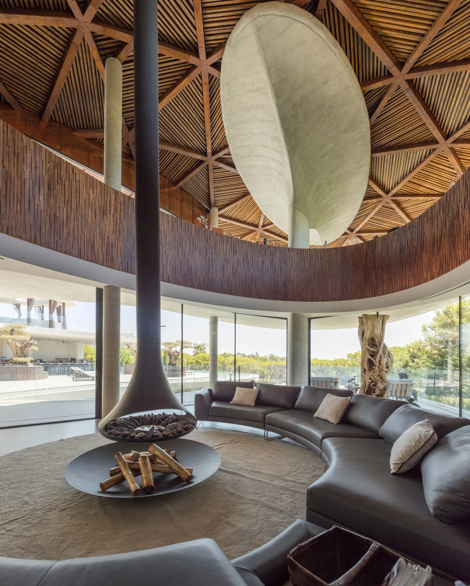 Living space with an intricate wooden ceiling design featuring a suspended fireplace and rounded sofa