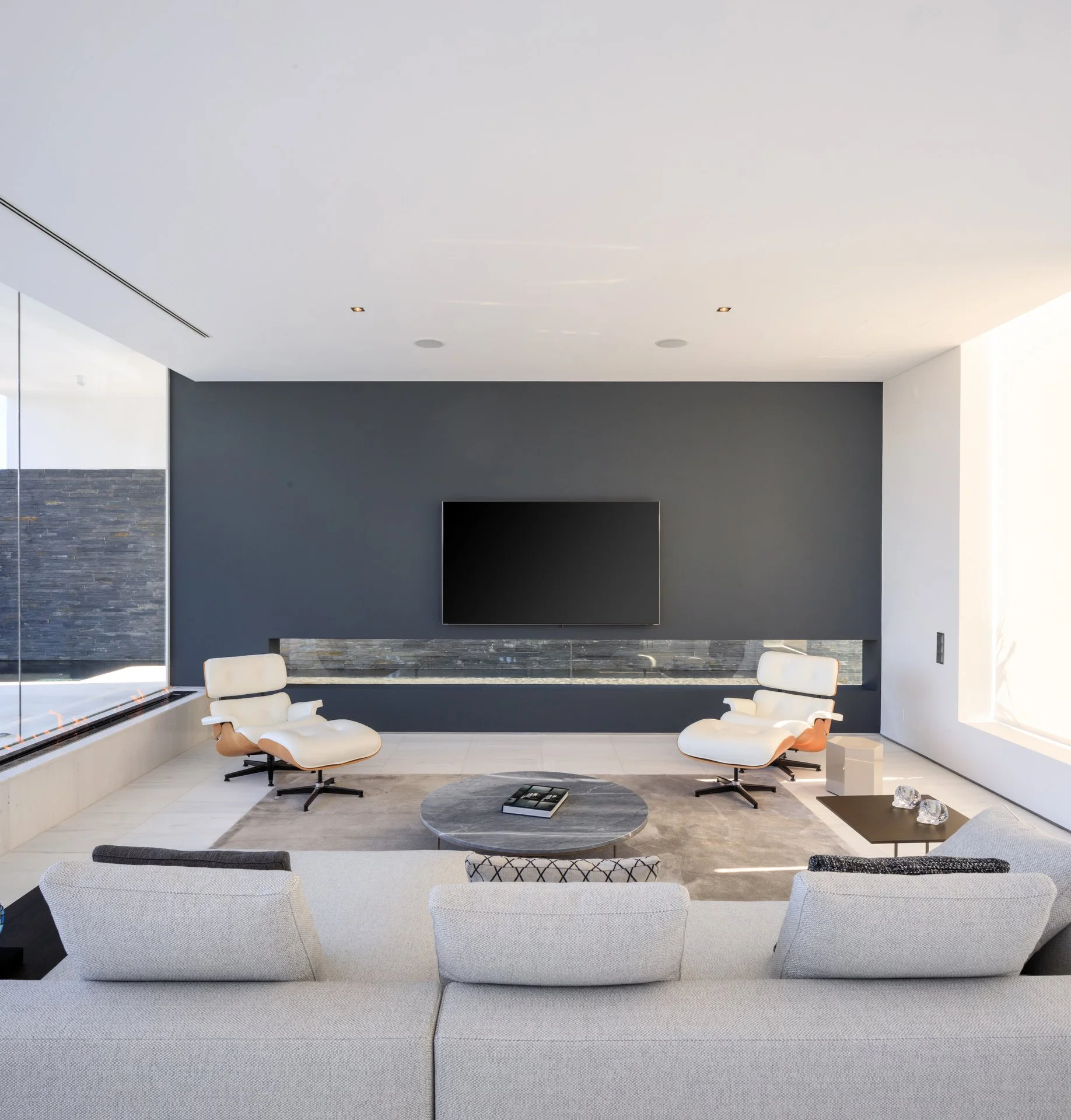 Cozy living room with luxury interior design, including a white sofa and two lounge chairs with a marble coffee table and TV stand