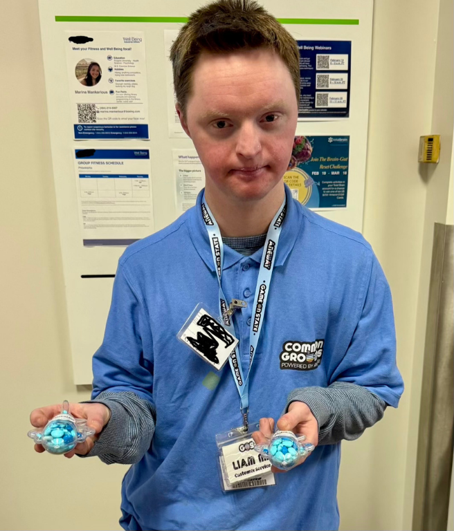 A yound man with red hair wear a blue ANEWAY shirt holds two turtle containers filled with blue candies