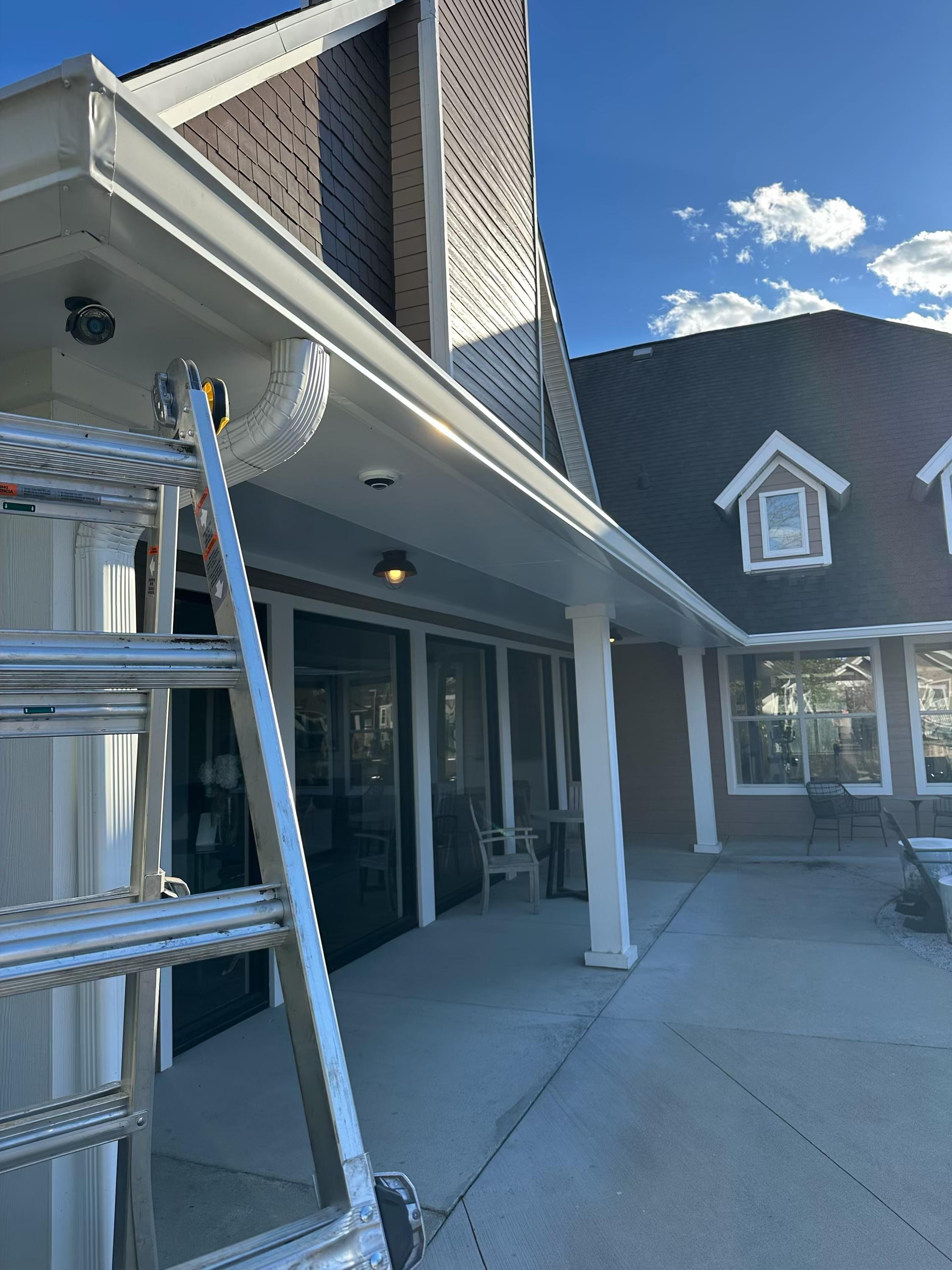 View of a house exterior with a back porch, ladder, and gutter system. Clear blue sky with a few clouds.