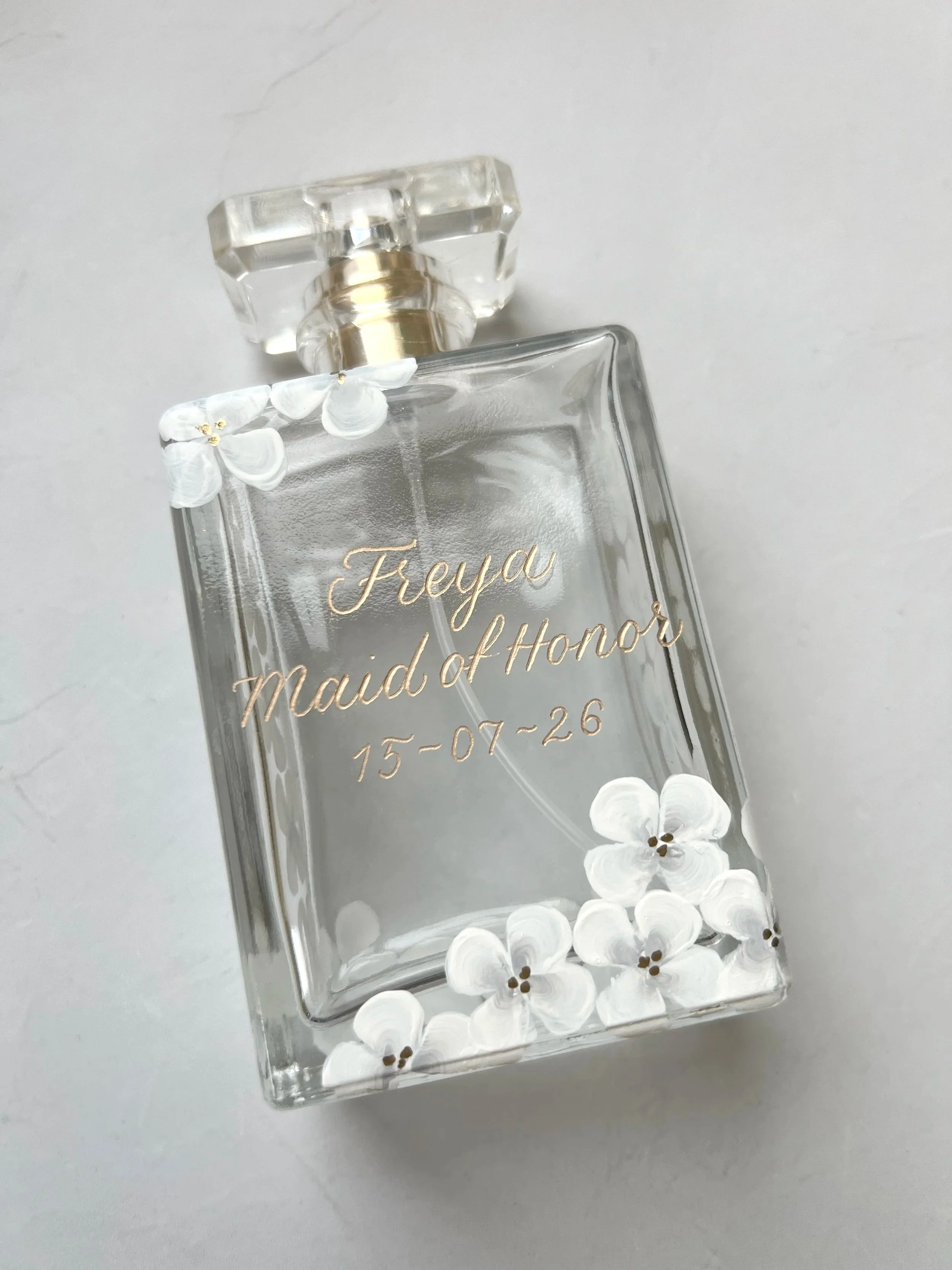 Minimal personalised perfume bottle with white floral detailing and gold calligraphy name and date
