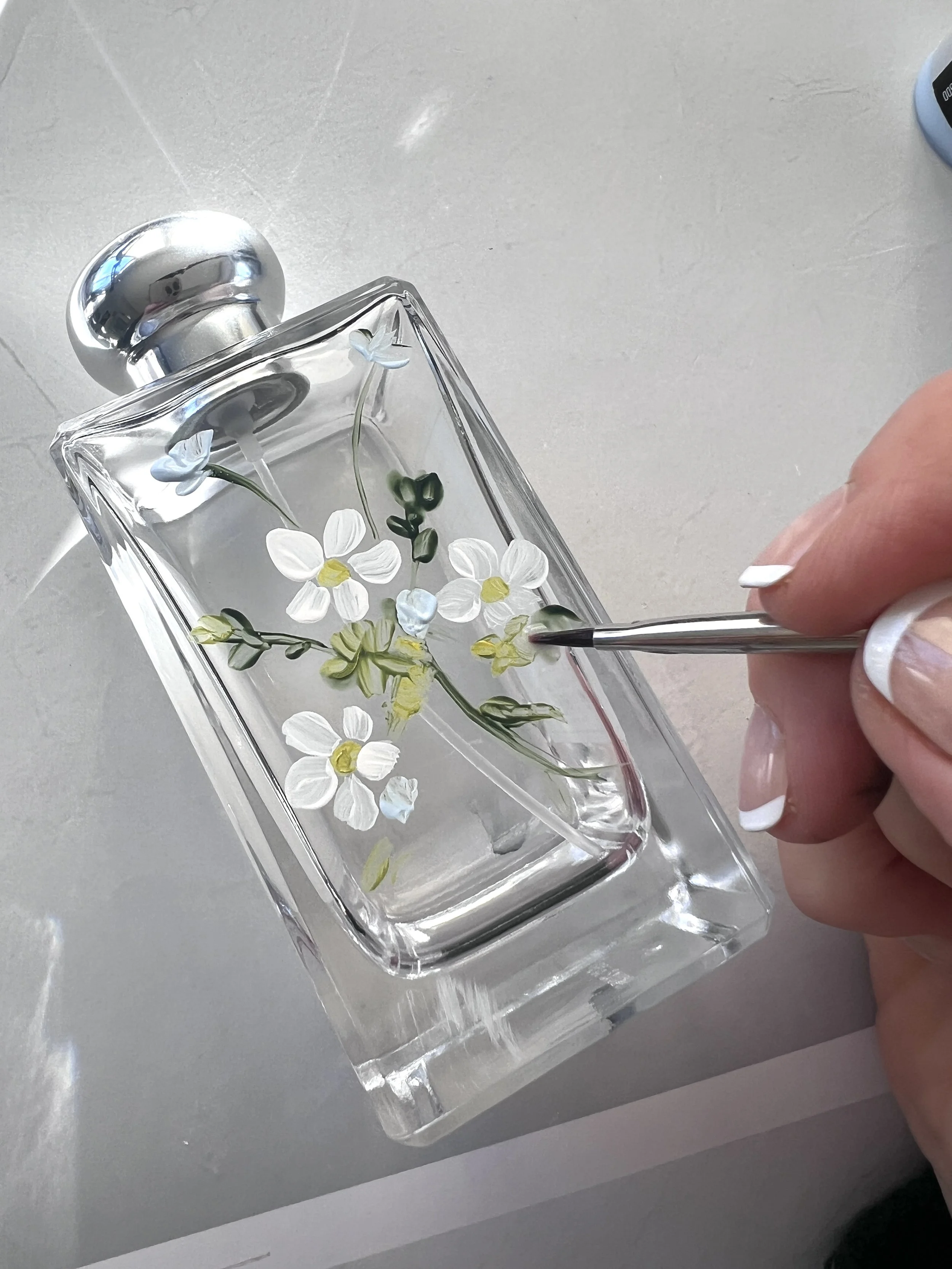 Hand painting white daisies onto a clear glass perfume bottle