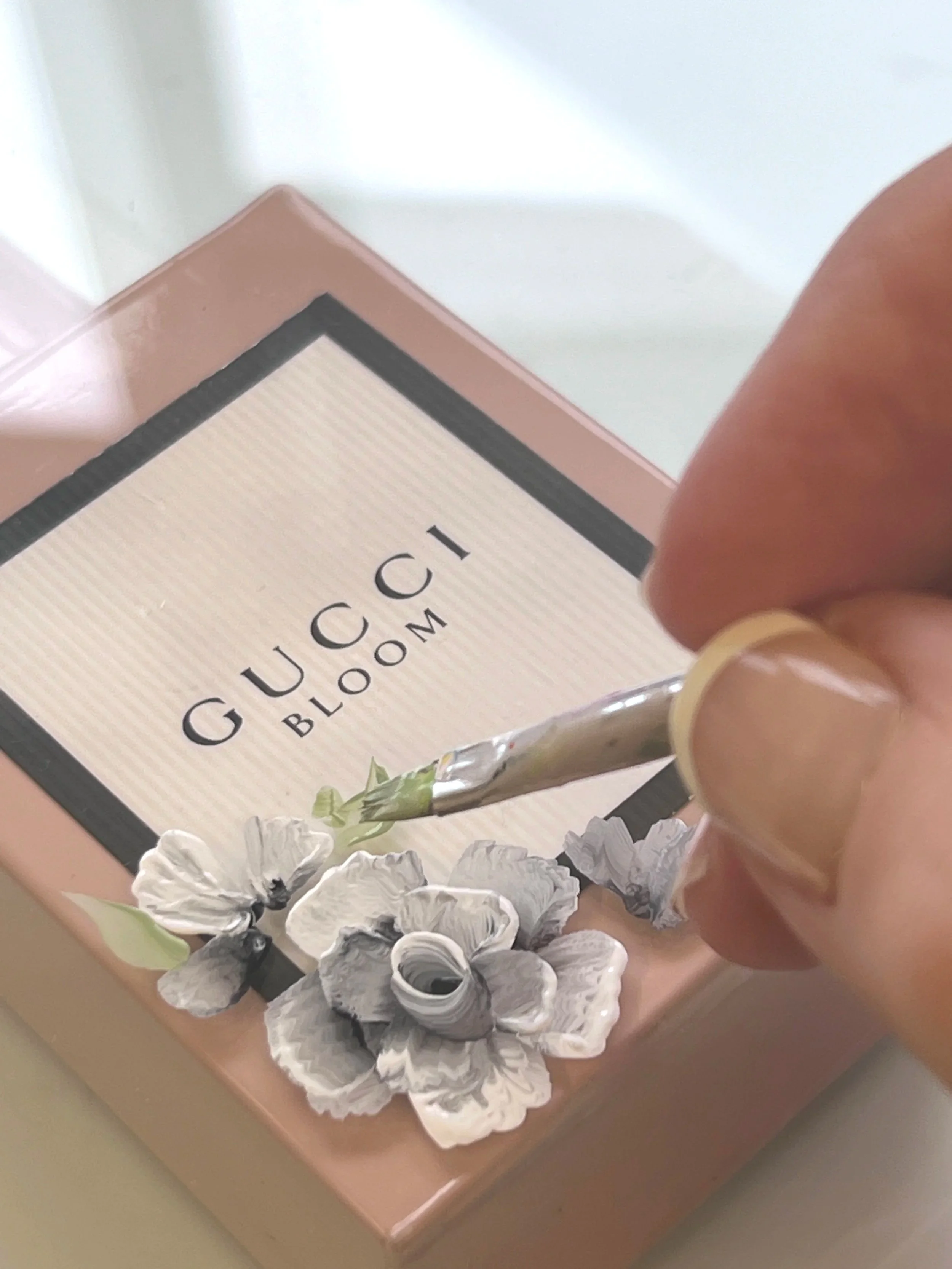 Hand-painted floral detailing in progress on a Gucci Bloom perfume bottle, prepared in the studio.