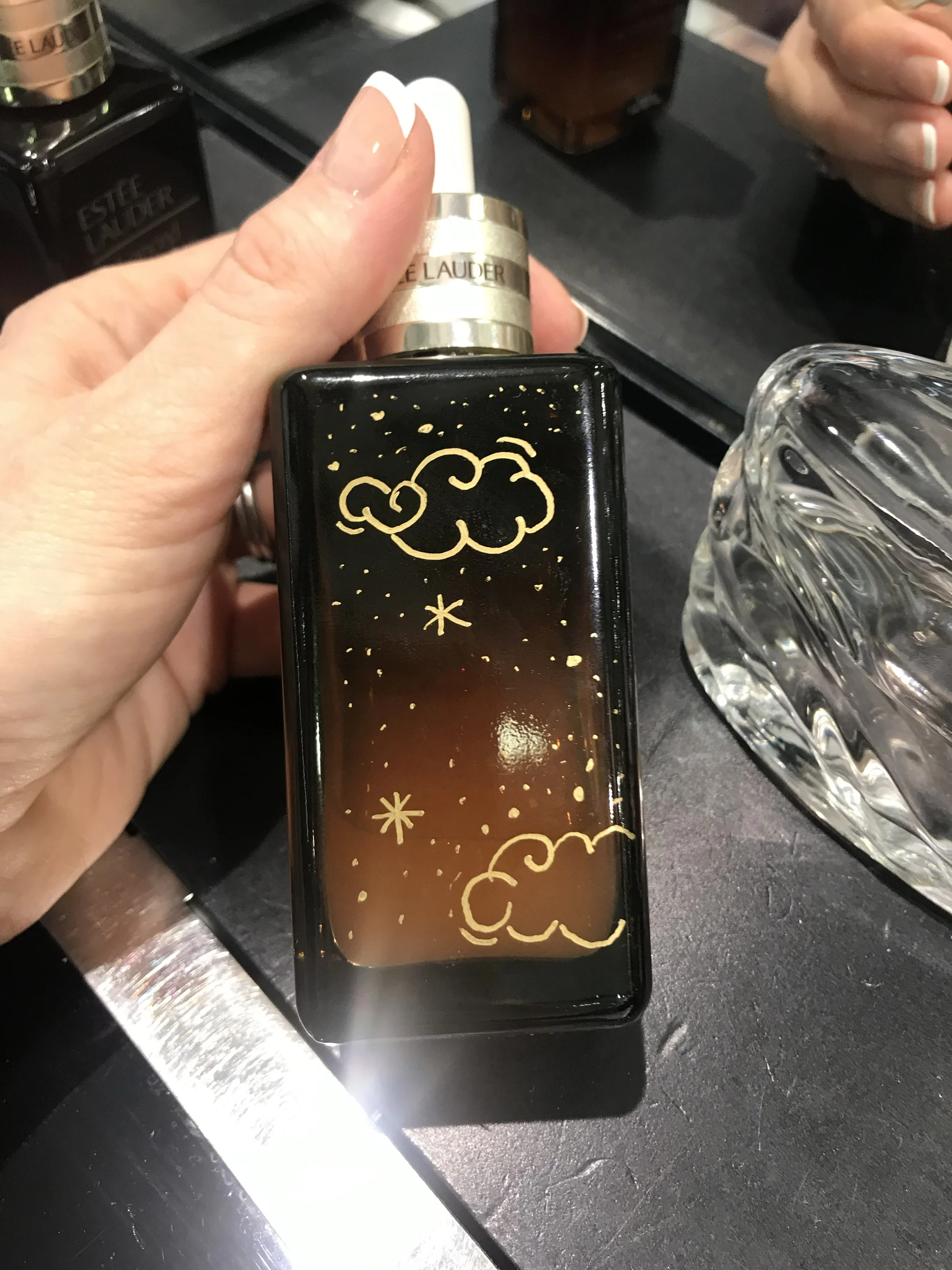 Live hand illustration of clouds and stars on Estée Lauder bottle at a brand activation