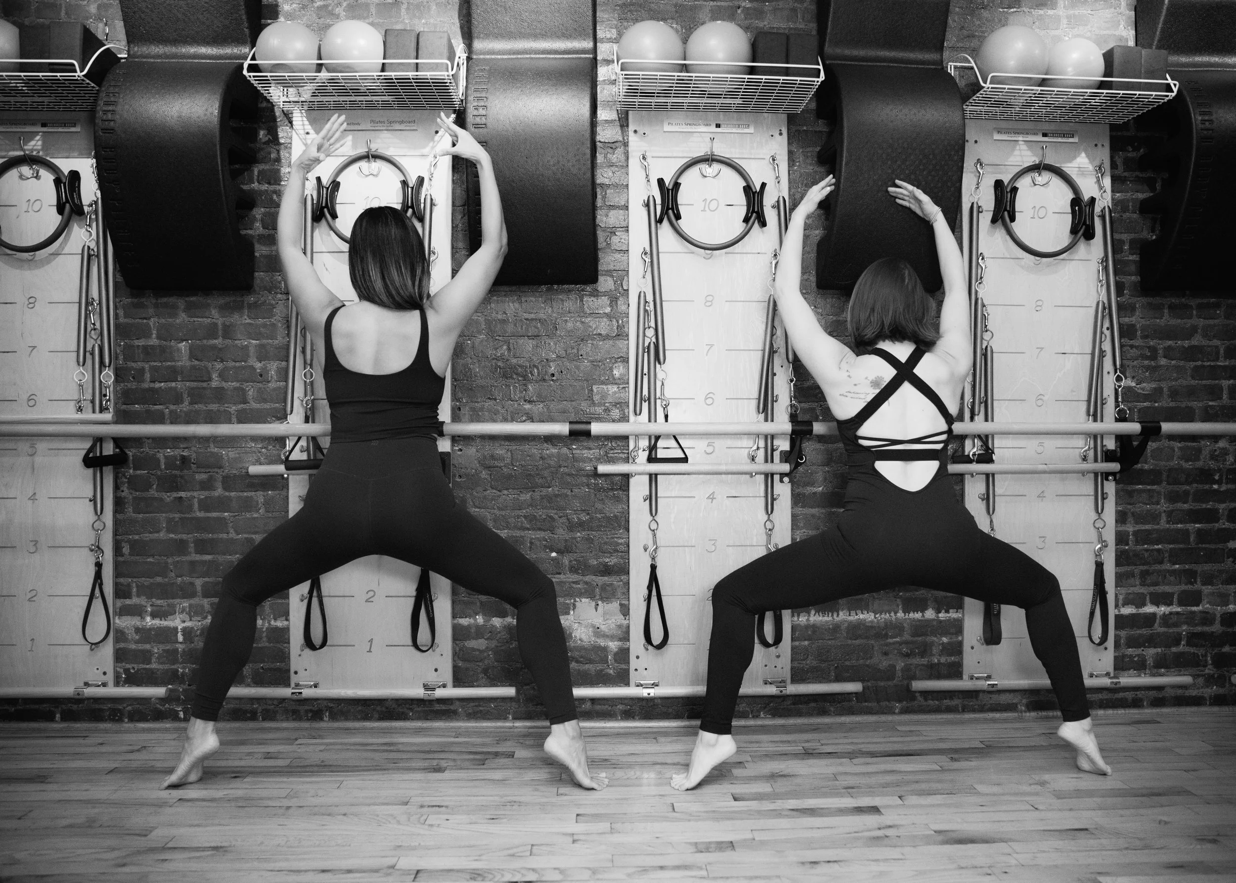 Two women practicing Pilates exercises using wall-mounted equipment in a fitness studio.