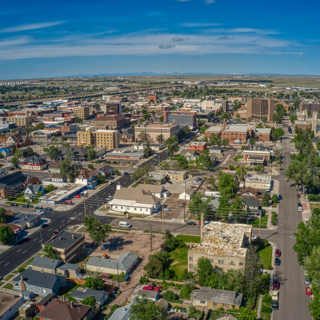 Aerial view of a small city with a mix of residential and commercial buildings, streets, and trees under a partly cloudy blue sky.