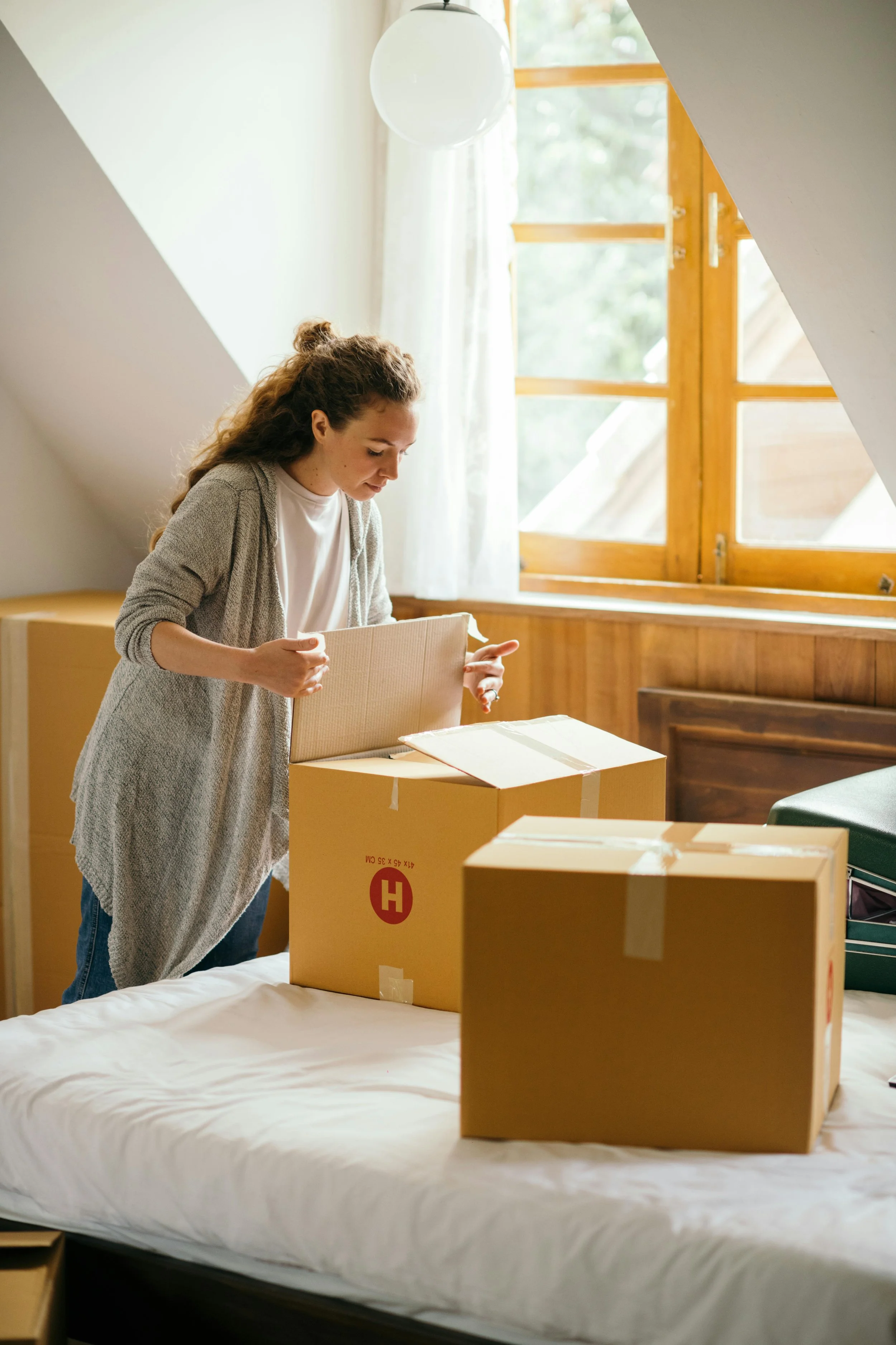 Woman unpacking cardboard boxes in a bright room with a window.