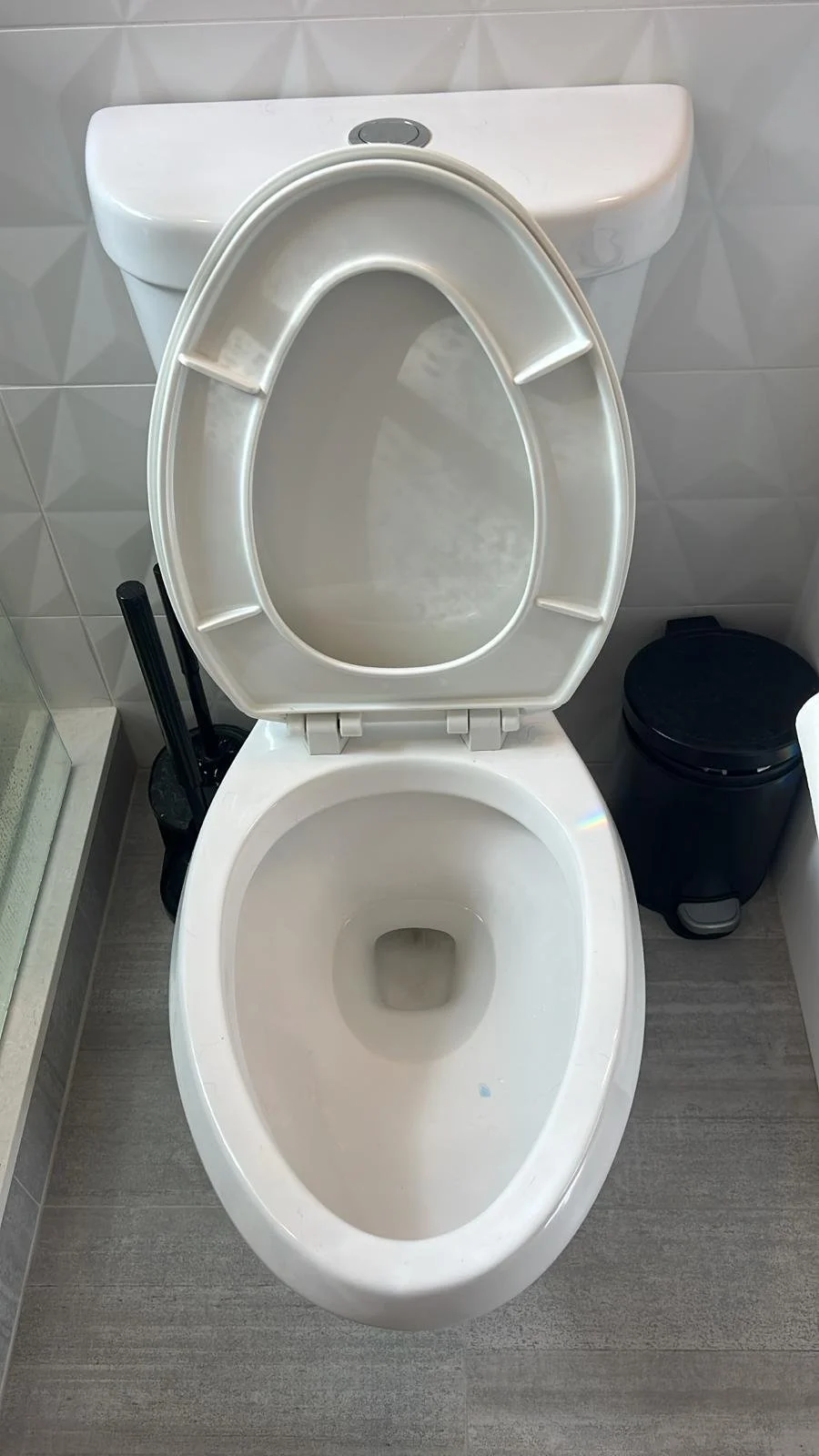 Toilet with the lid open in a bathroom, with toilet cleaning tools and trash bin nearby.