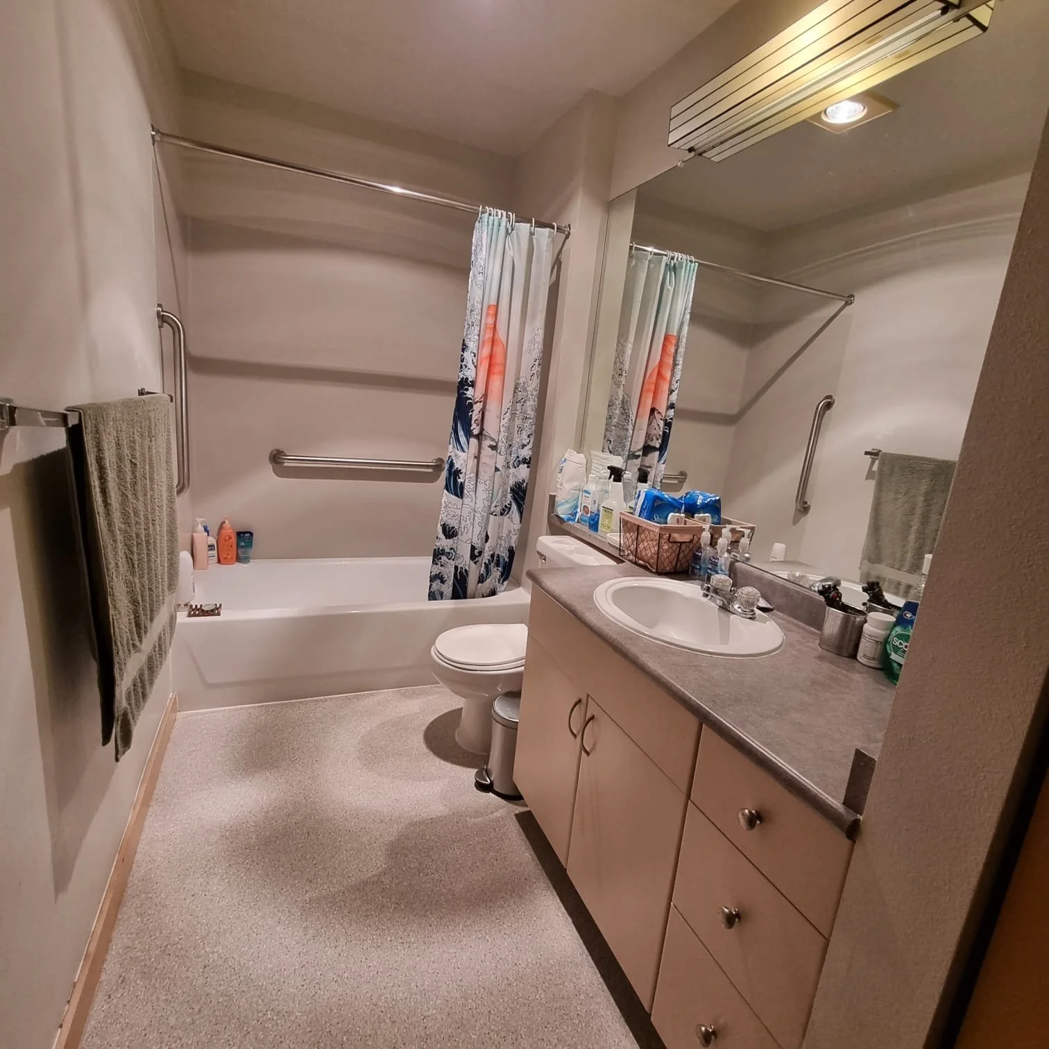 A bathroom with a bathtub and shower on the left, a towel hanging on a rail, a vanity with a sink, a mirror, and various toiletries on the counter.