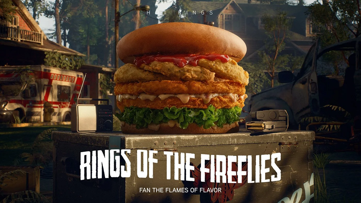 A giant burger with layers of fried chicken, lettuce, sauce, and fried onion rings, placed on a metal container outdoors with trees, a fire truck, and a car in the background.
