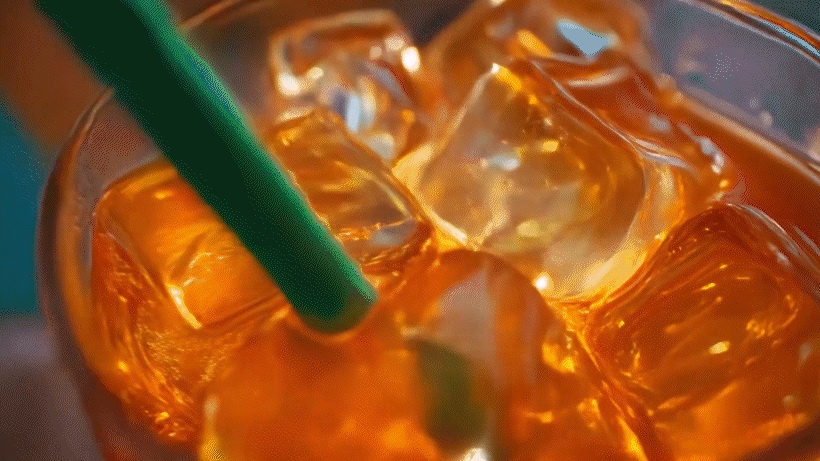 Close-up of a glass filled with iced tea, ice cubes, and a green straw.